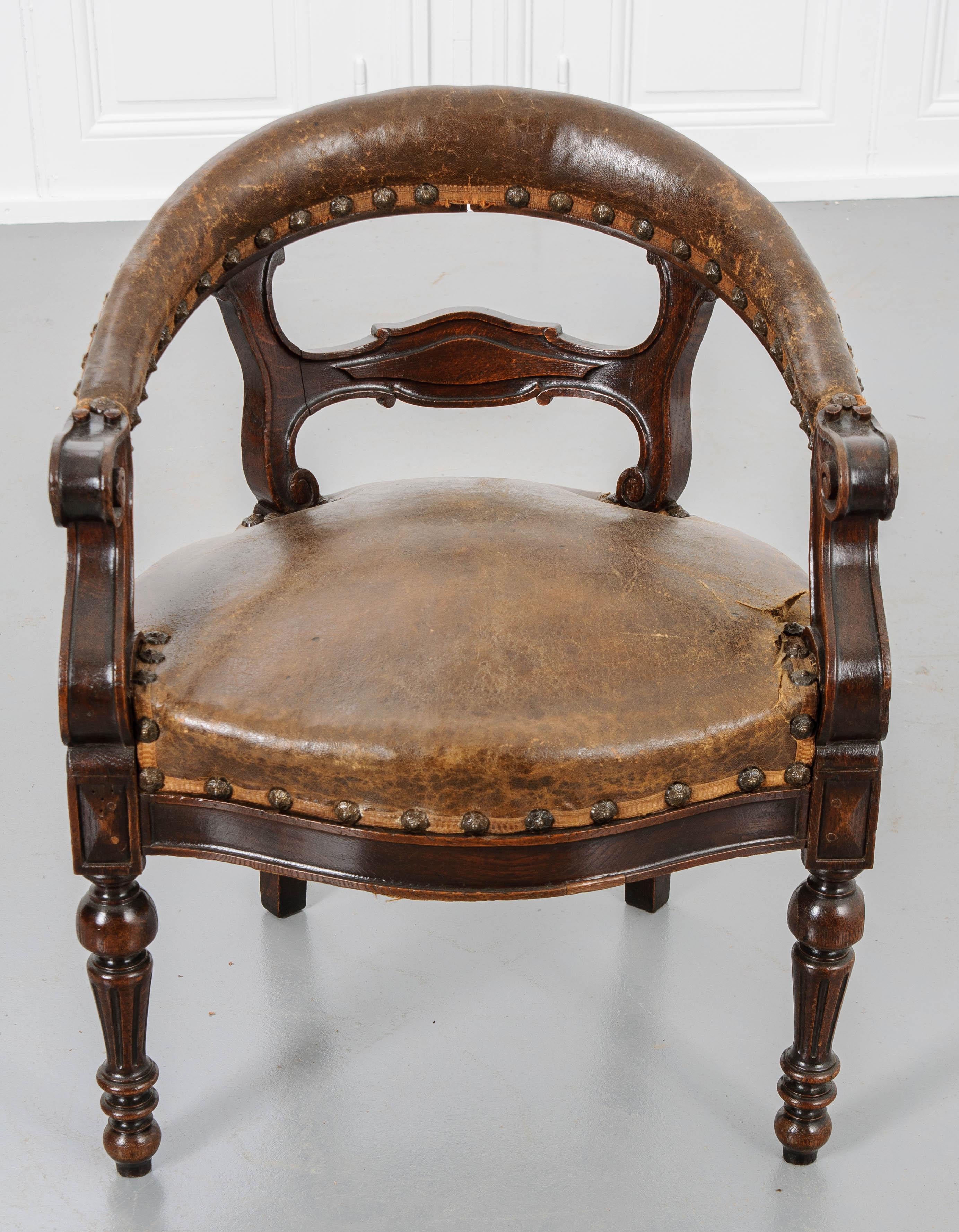 This handsome tub chair, c. 1830, is made of beautiful English oak and has wonderfully aged leather upholstery.  The clean wood finish juxtaposed against the patinated leather and architectural nail heads make for an attractive chair.  Sit into the