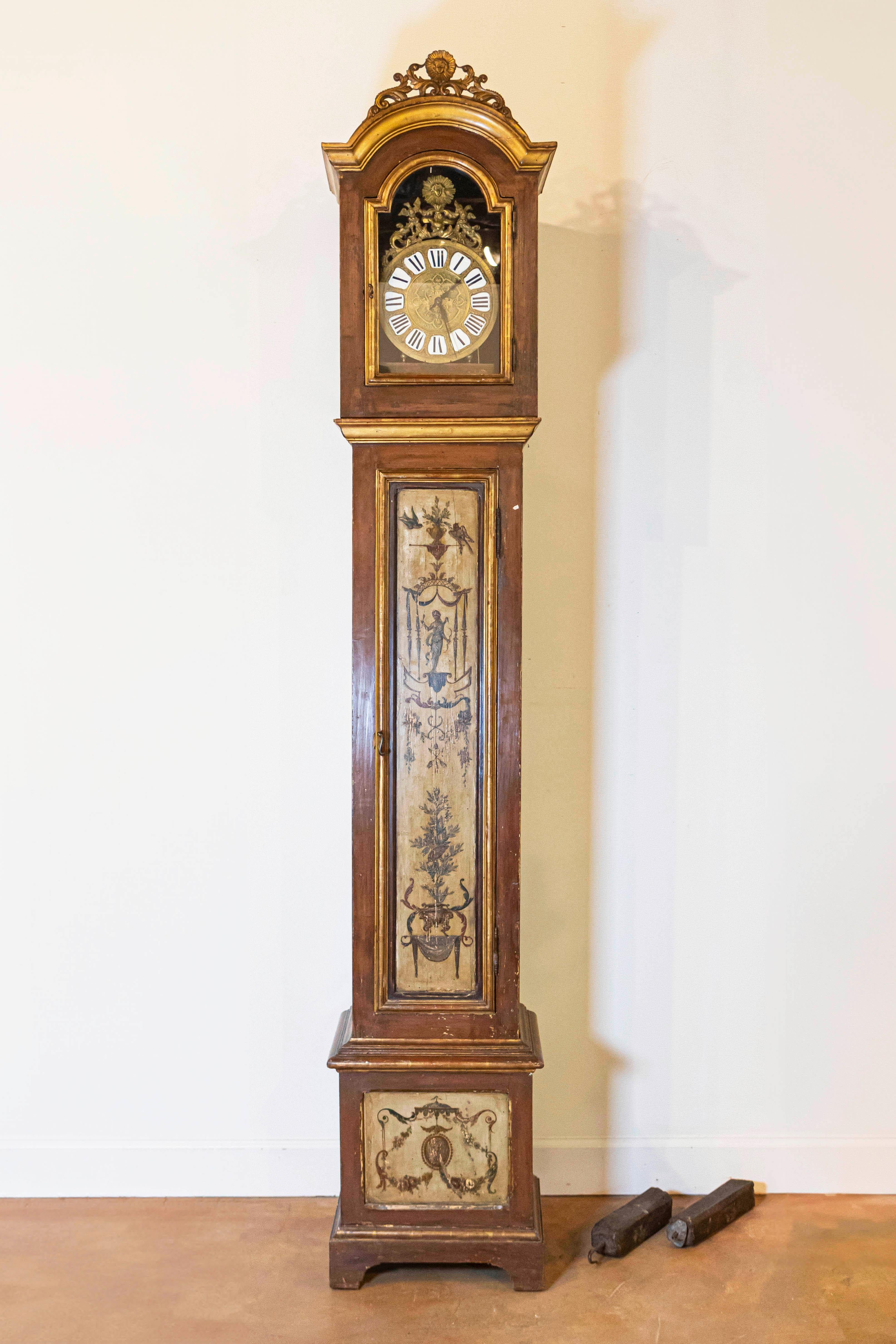 A French parcel gilt and red painted longcase grandfather clock from the 19th century, with carved crest and classical décor. Born in France during the early years of the 19th century, this long case clock features a rectangular head, adorned with a