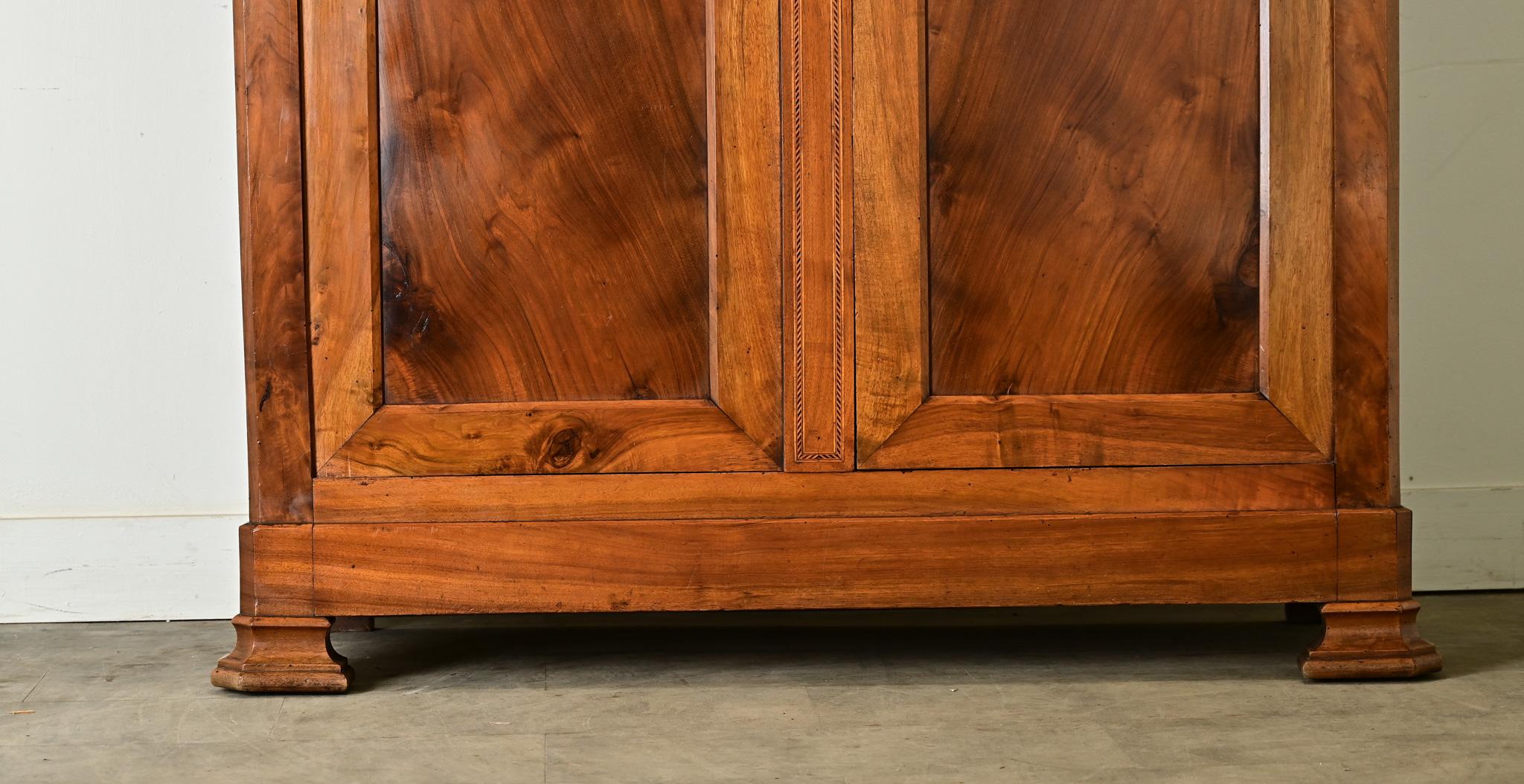 A monumental French 19th century Louis Philipe armoire of stunning walnut construction. Crowned with an understated cornice, two paneled doors show classic arches at the top like doorways, drawing the viewer in. Bookmatched walnut on the door