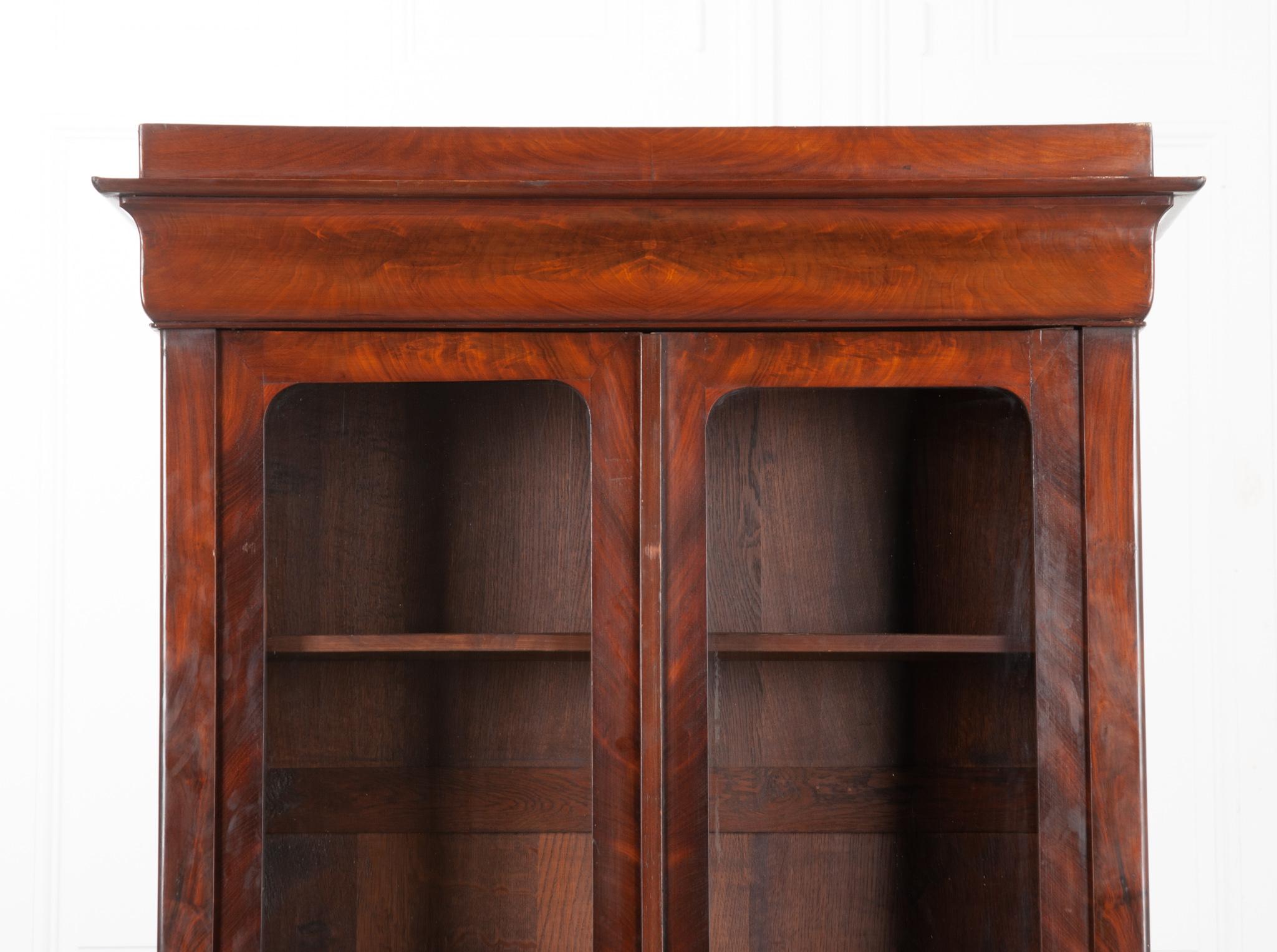 This is a handsome Louis Philippe bibliotheque from 19th century France. Made of rich bookmatched mahogany for a great symmetrical look. The crown is 14”D, the body is a little slimmer at 12”D. The doors feature the original wavy glass and a