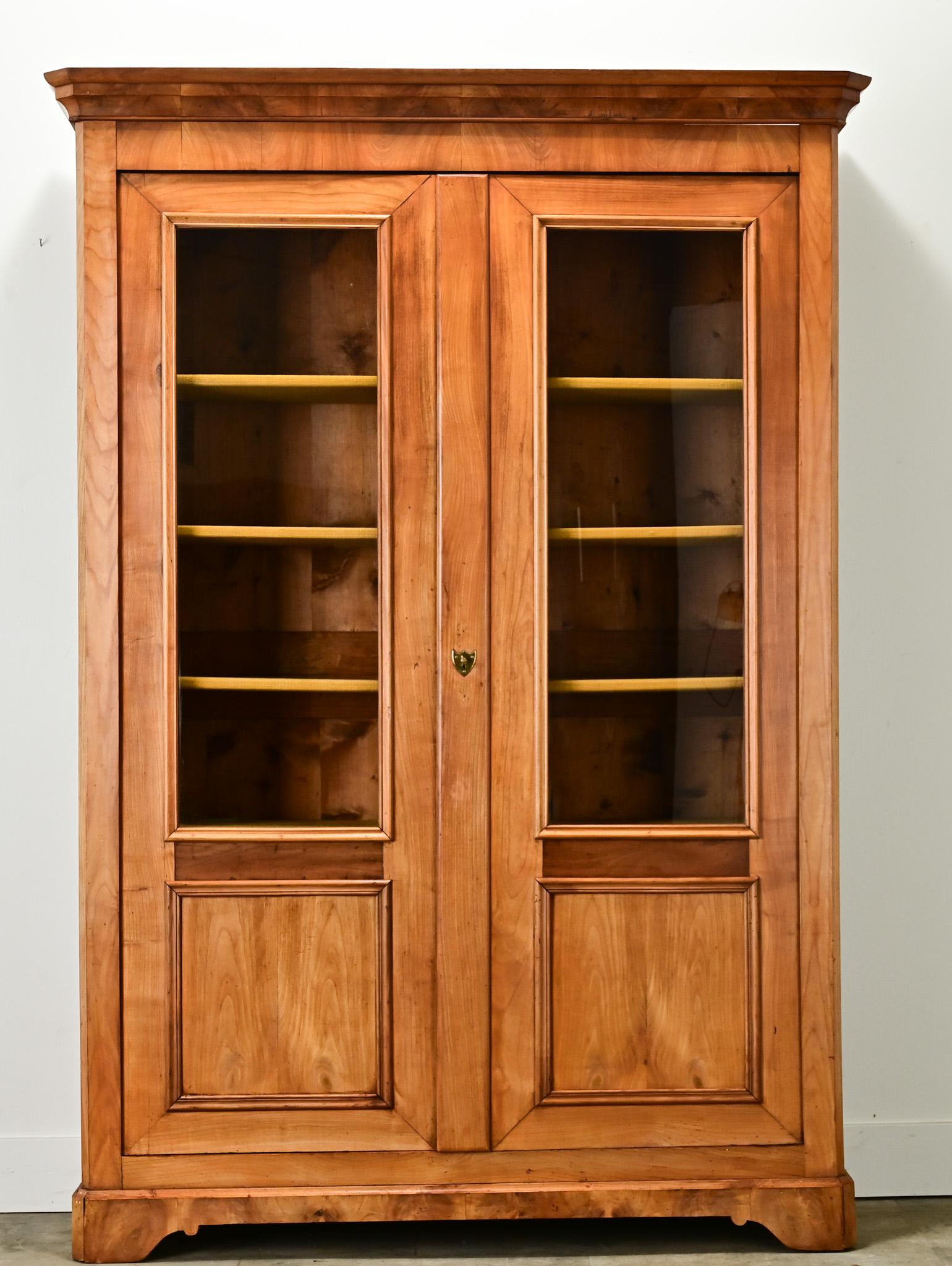 A handsome French Louis Philippe bibliotheque made of blonde mahogany. There are two paneled cabinet doors with new glass at the top that open with a functioning lock and key. The interior has four fixed pine shelves wrapped with a custom mustard