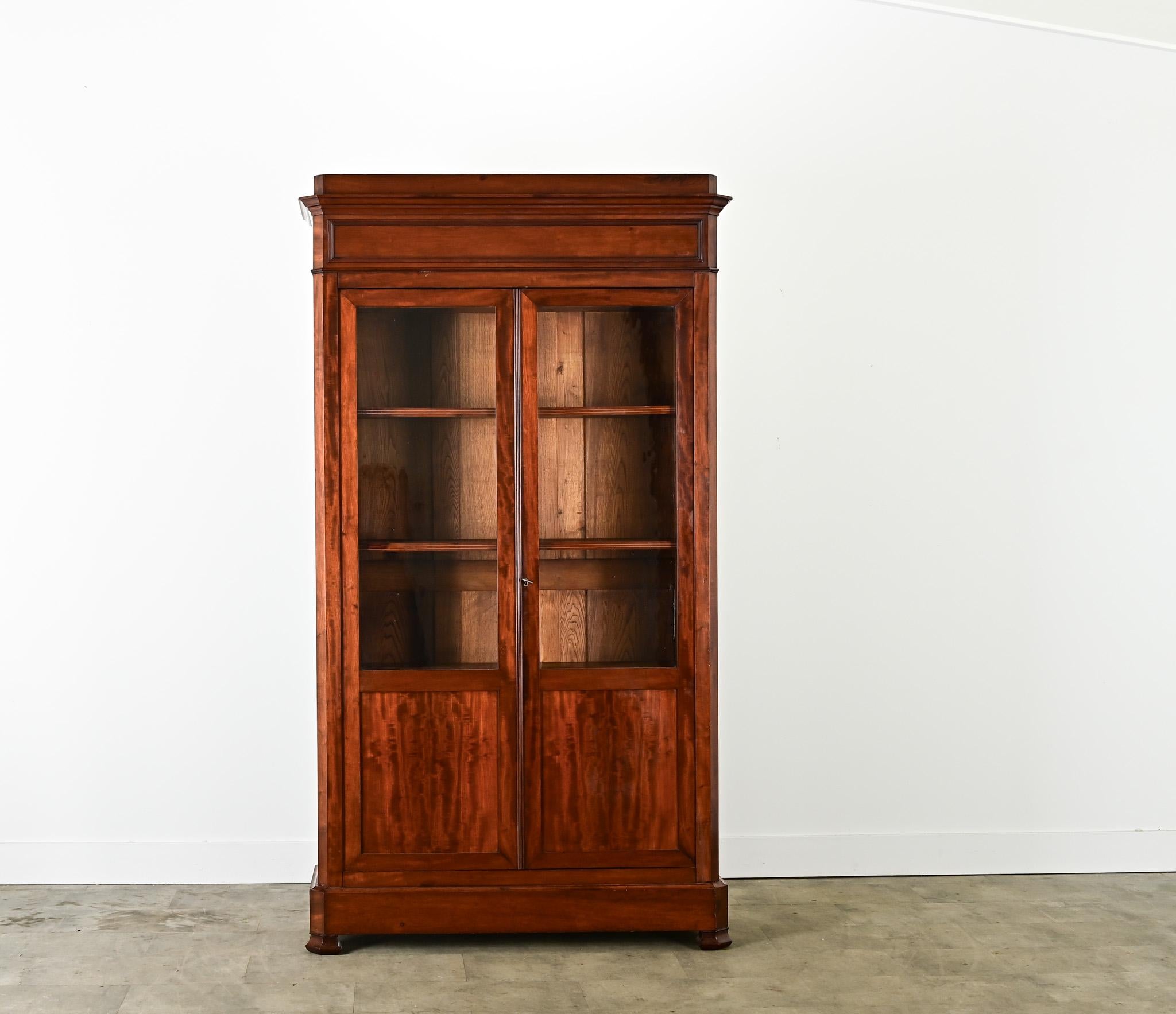 A 19th century French Louis Philippe style bibliothèque or bookcase, handcrafted of timeless mahogany with two glass-front doors for displaying treasured books, heirlooms, or trophies in an office or library. The clean, straight lines allow this