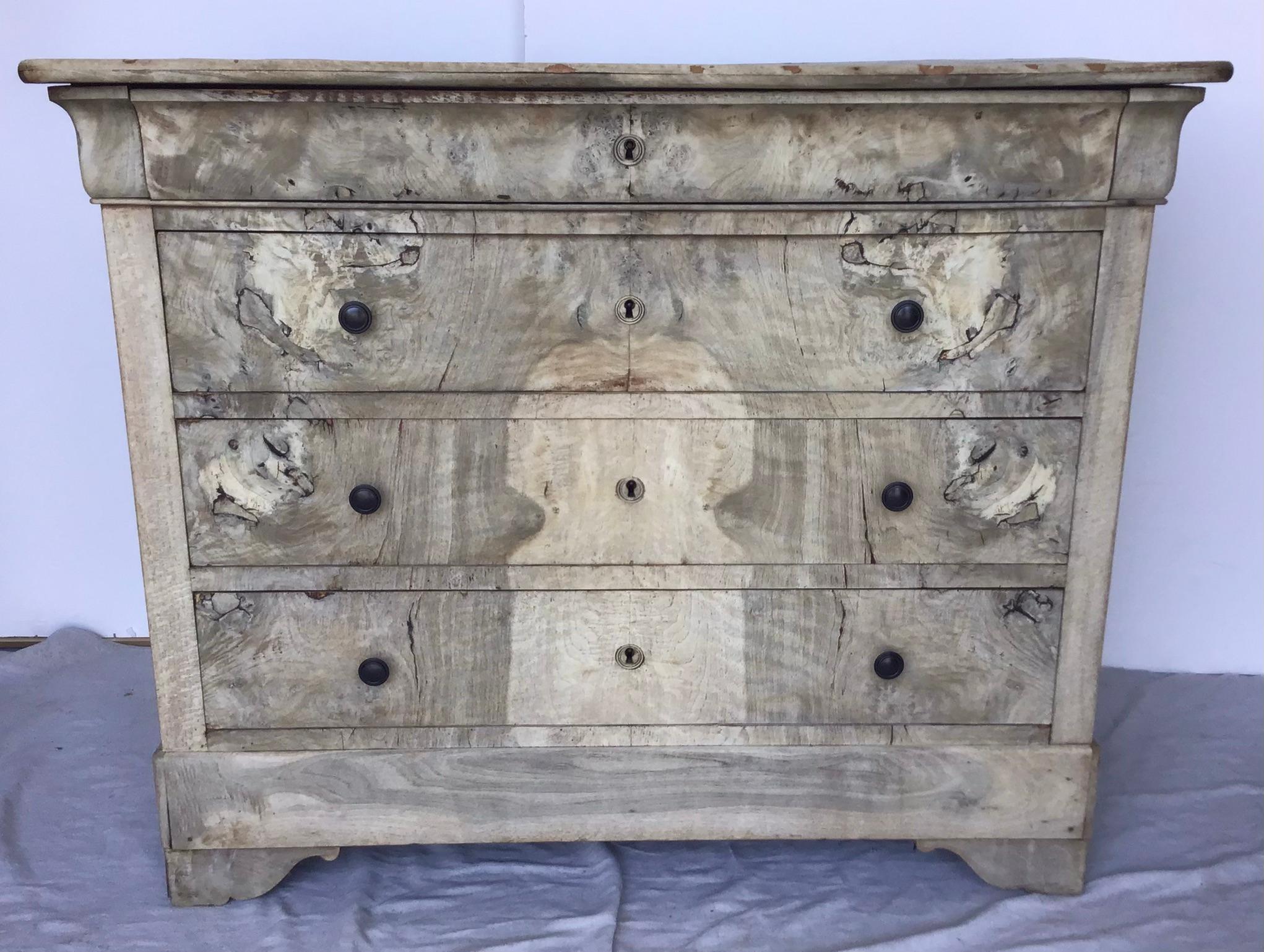 A French Louis-Philippe style bleached burl wood commode from the late 19th century. This Louis-Philippe commode features an exquisite bookmark veneer burl façade. A narrow frieze drawer sits above three additional dovetailed drawers, larger in
