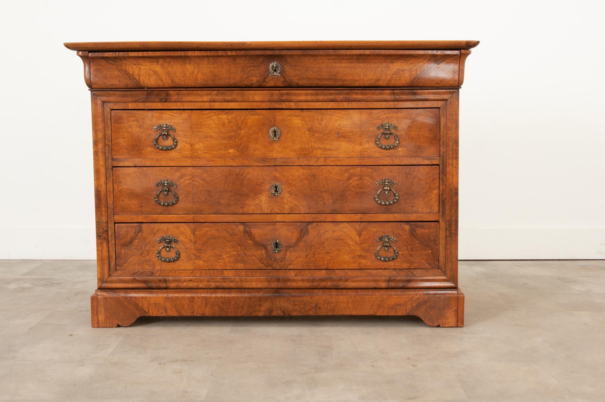 A French Louis Philippe burl and bookmatched mahogany commode is in wonderful antique condition. There are four working locks surrounded with gilt bronze escutcheons, 1 key is used for all locks. Three of the large drawers have recently added Empire