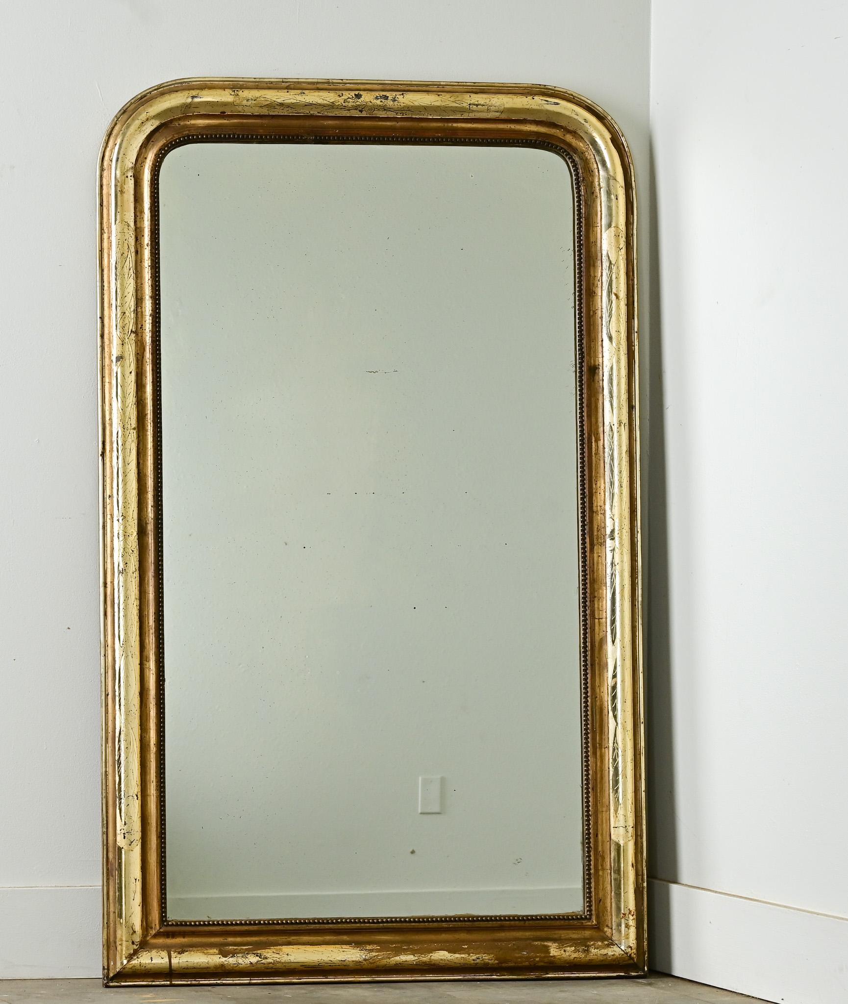 Tall and slender leaves in matte and polished gold unfurl across the carved giltwood frame of this Louis Philippe mirror. The Japonisme influence is lightly concealed by oxidation and patina darkening the gilt. The original mirror plate is lightly