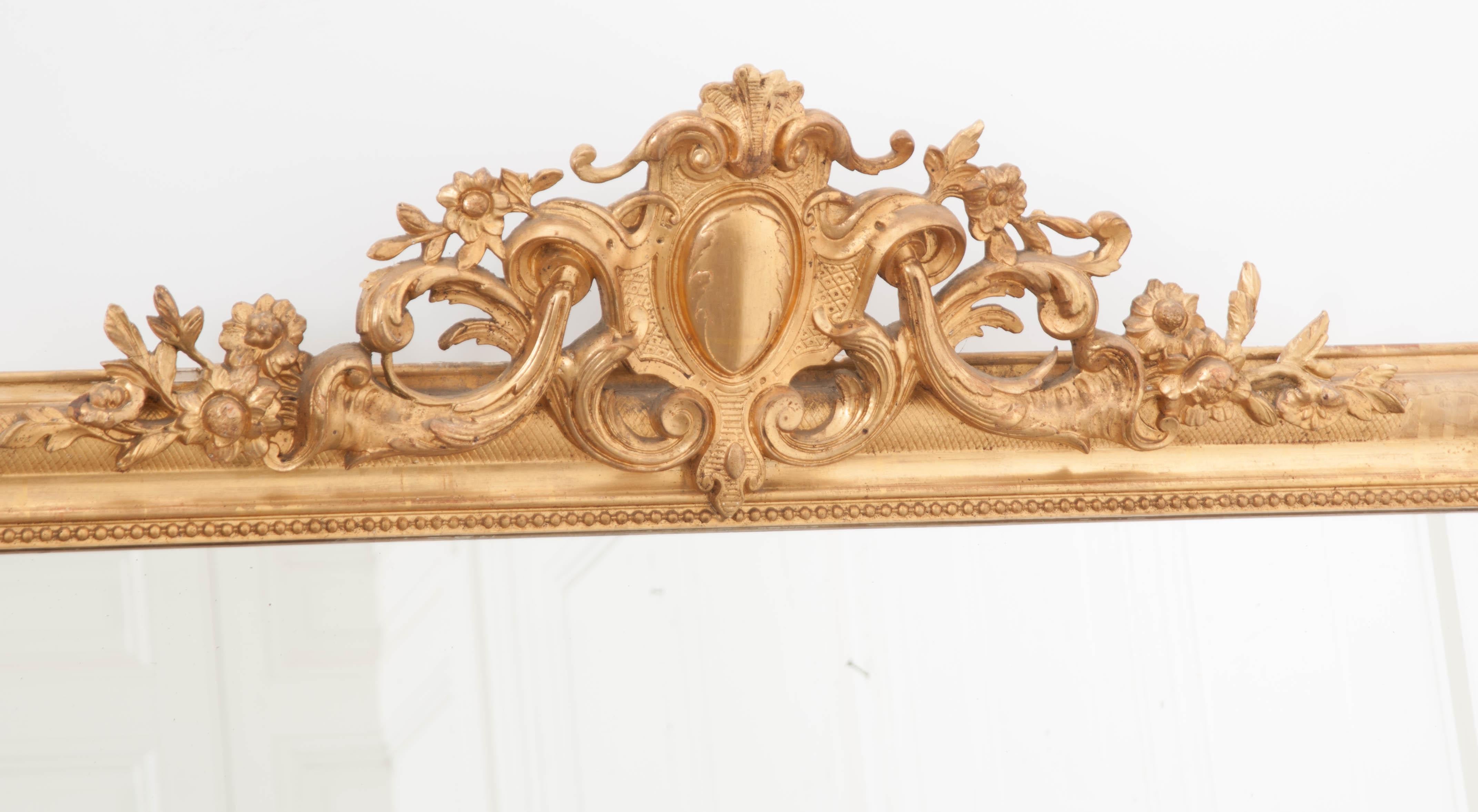 This grand, yet refined, Louis Philippe giltwood overmantel mirror is from 1830’s France and features an intricately carved crest centered by an egg-and-scroll cartouche flanked by scrolling floral vines. The carved frame has rounded upper corners,