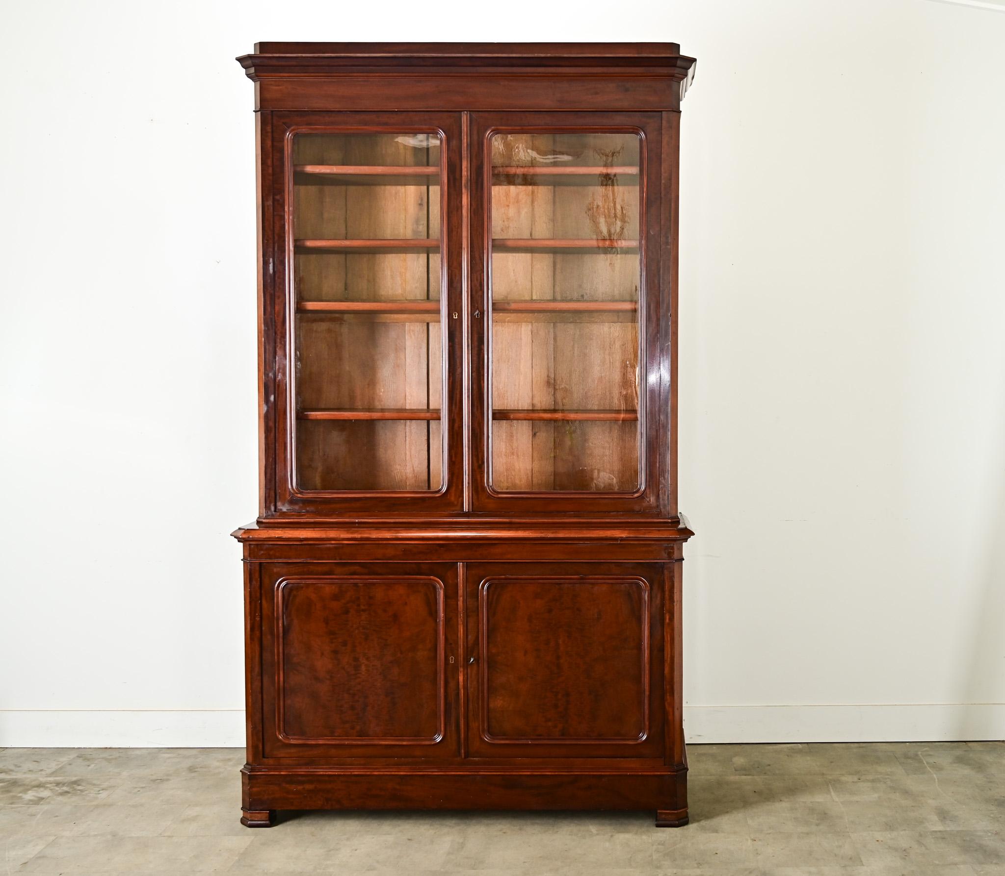 A substantial 19th century French Louis Philippe style bibliothèque or bookcase, handcrafted of mahogany with a lovely sheen that reveals variegated colors and grain patterns in the wood. Behind the locking doors–which appear to have retained their