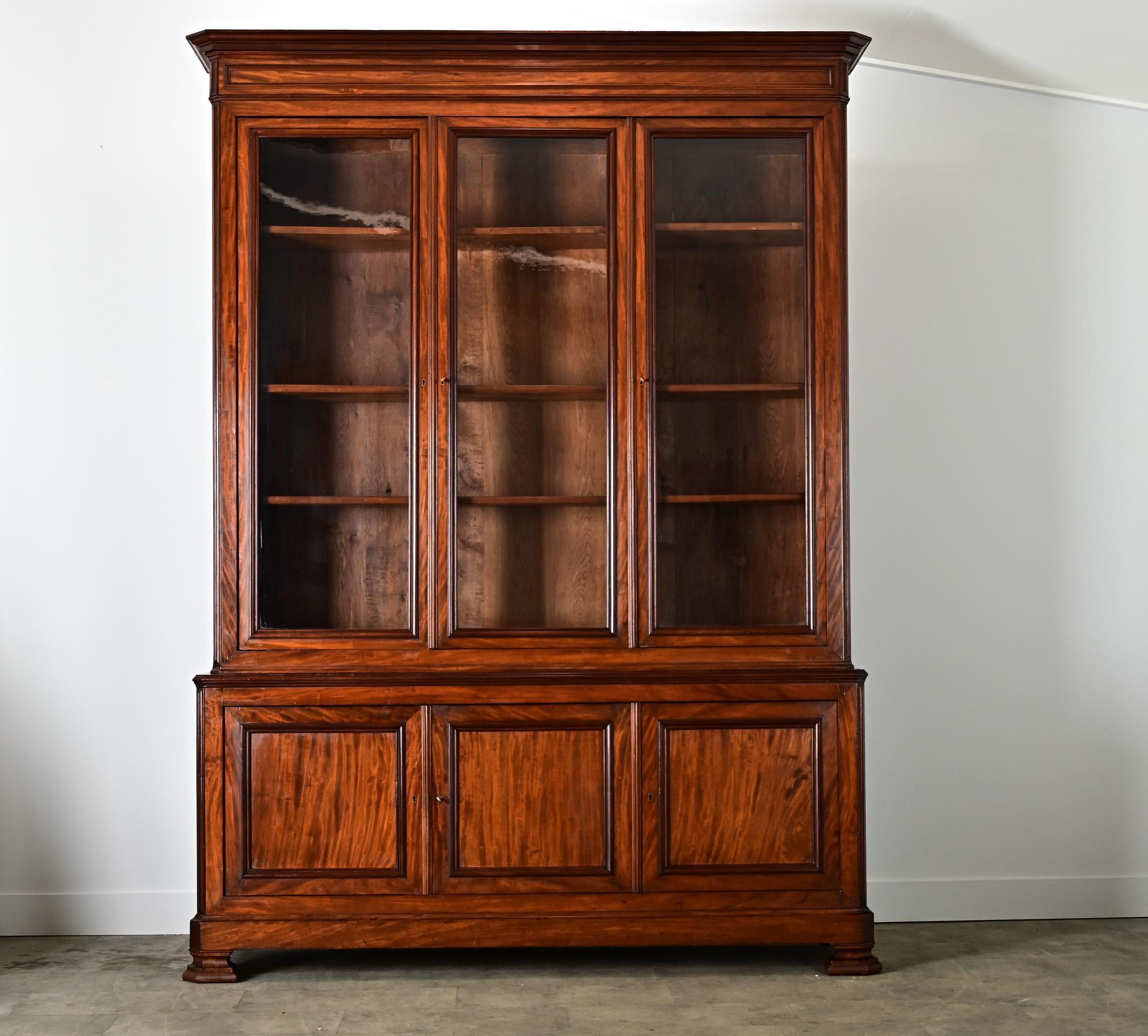 Une imposante bibliothèque de style Louis Philippe du XIXe siècle, fabriquée à la main en acajou, avec trois portes vitrées pour exposer des livres précieux, des objets de famille ou des trophées dans un bureau ou une bibliothèque. Les lignes