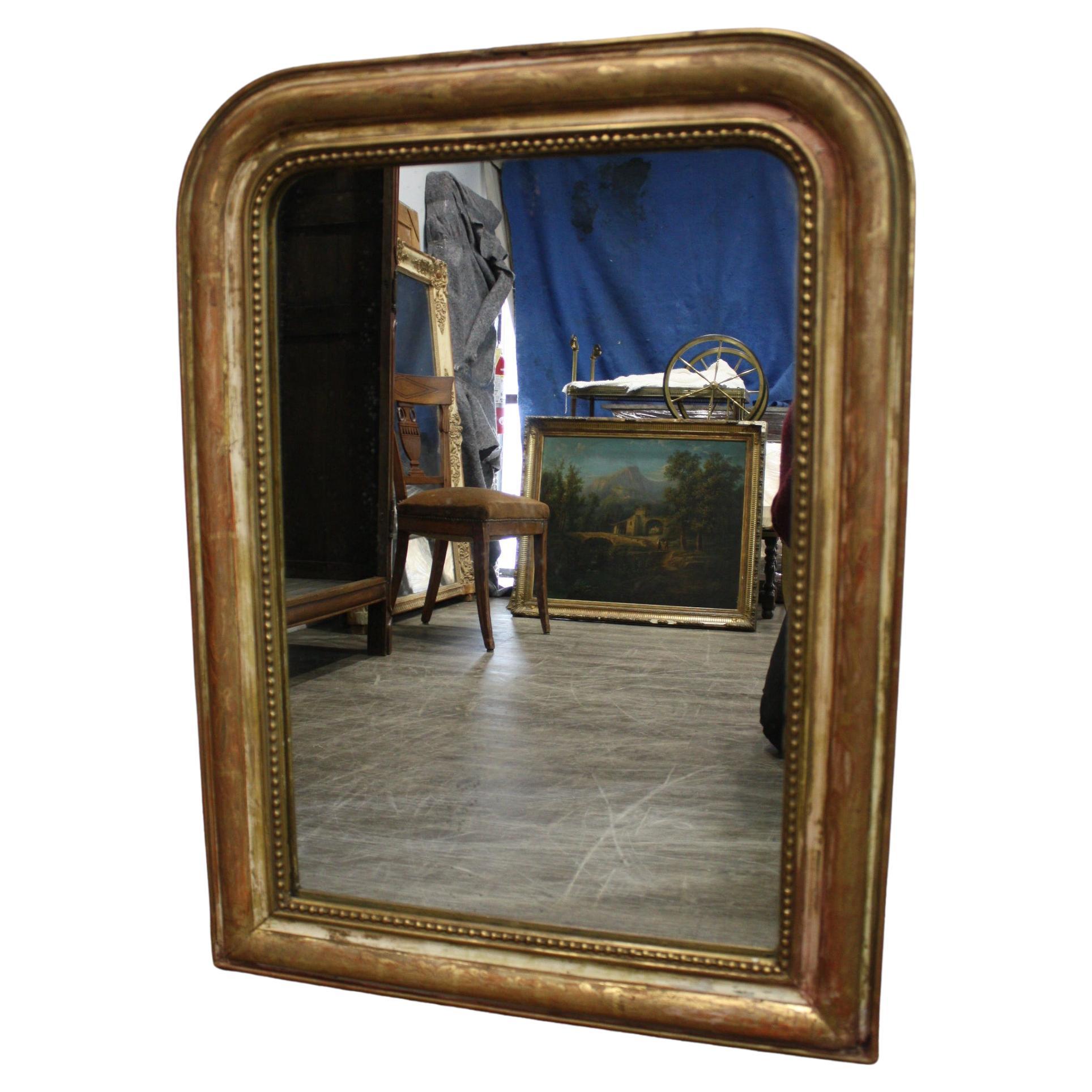 Ce miroir est recouvert de feuilles d'or, il est partiellement décapé et le miroir en verre présente quelques usures.  taches dues à l'âge.