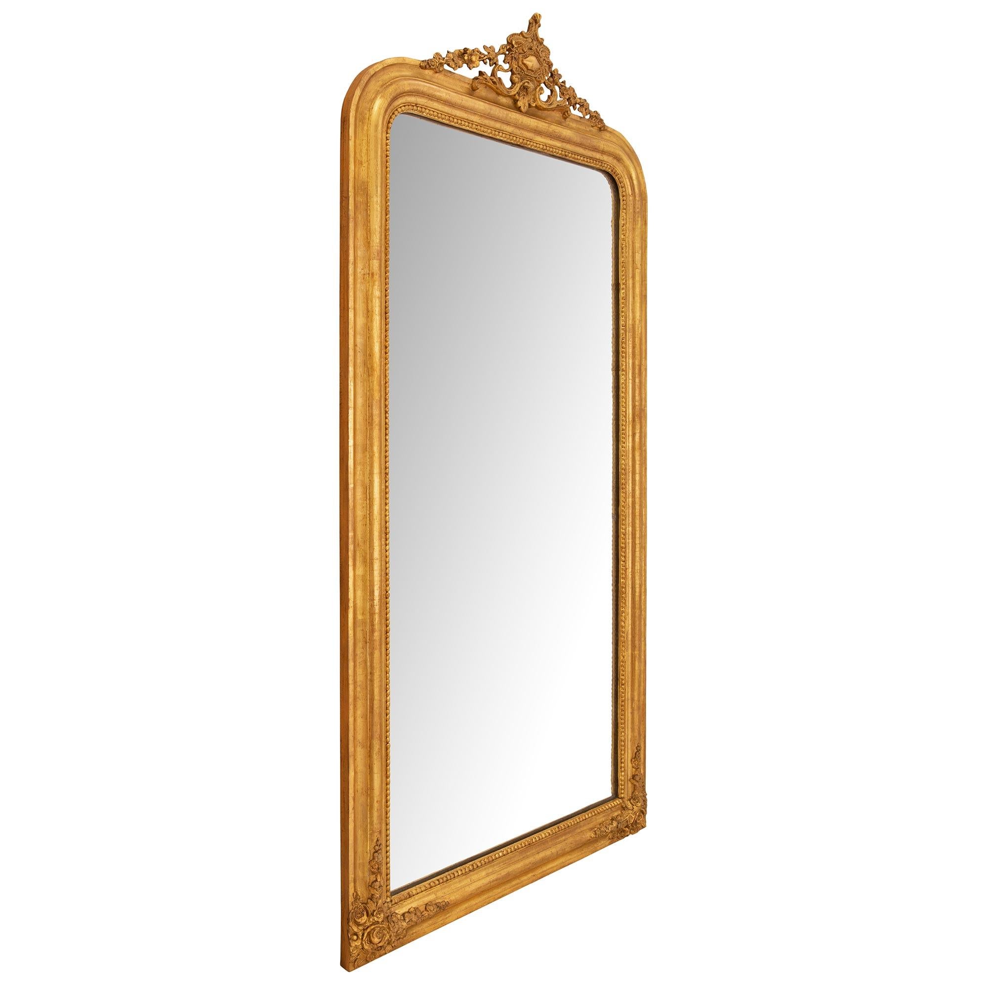 An elegant French 19th century Louis Philippe period giltwood mirror. The mirror retains its original mirror plate set within a fine wrap around beaded band. The mottled frame displays charming richly carved blooming flowers at each bottom corner