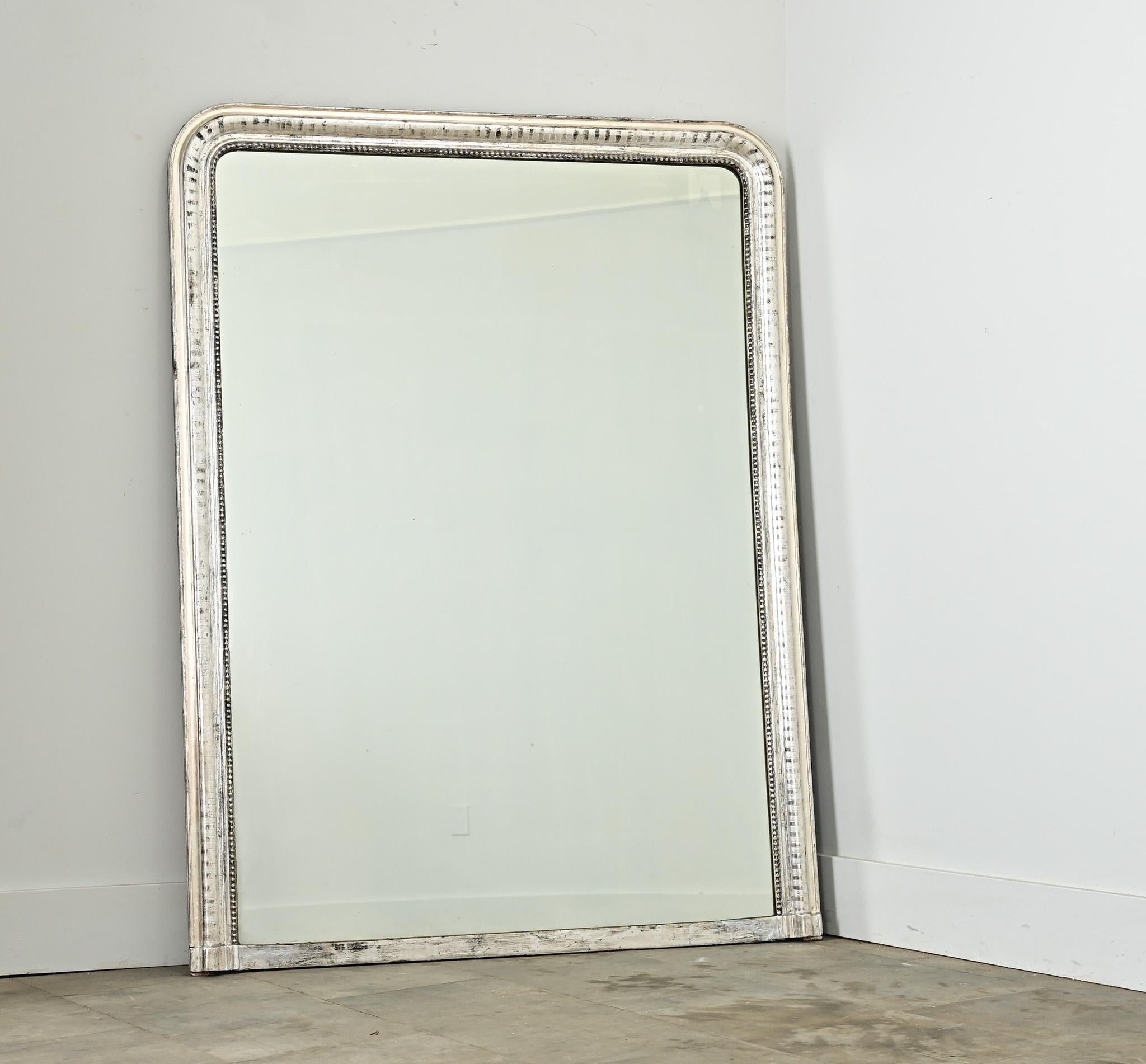Ordonné et d'inspiration architecturale, le cadre en argent doré de ce miroir Louis Philippe du XIXe siècle est méticuleusement gravé d'un motif en forme de pièce de monnaie le long du cadre arqué. La texture satinée est subtile et raffinée, et