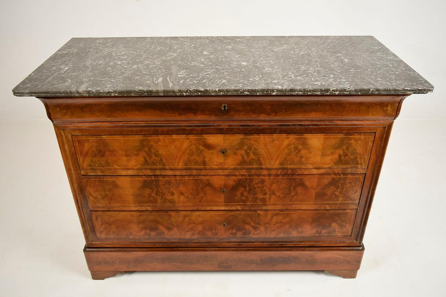 This 1830s French Louis Philippe-style chest of drawers is made from solid mahogany wood with its original stain finish. There are four drawers full size drawers that open with a lock and key. The chest is topped with a bevelled edge marble top in a