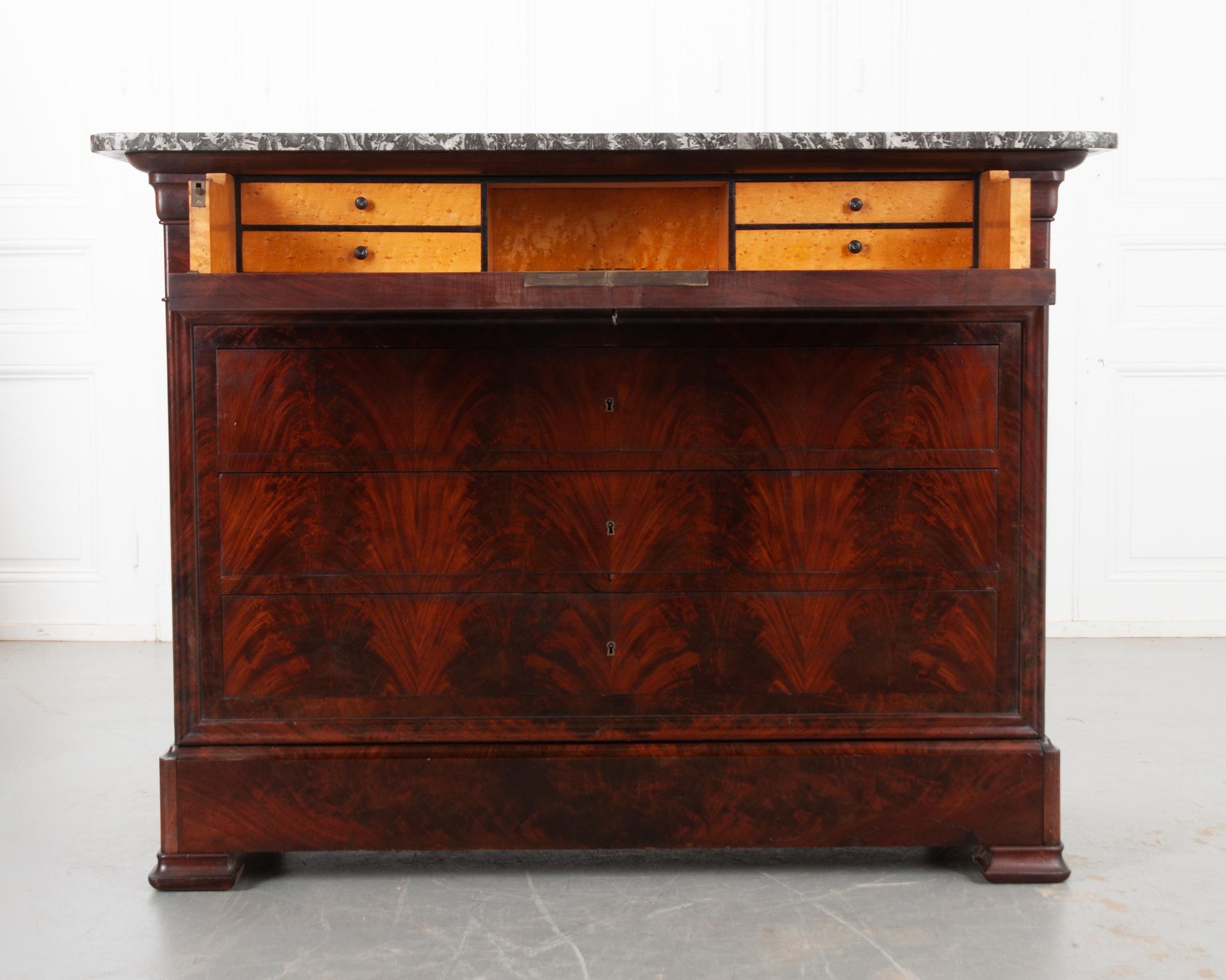 A stunning Louis Philippe style mahogany commode with a fold-down secretary desk housed in its top drawer. Its gray and charcoal marble top has rounded front corners and a fantastic visual texture, complimented by its exceptional mahogany finish.