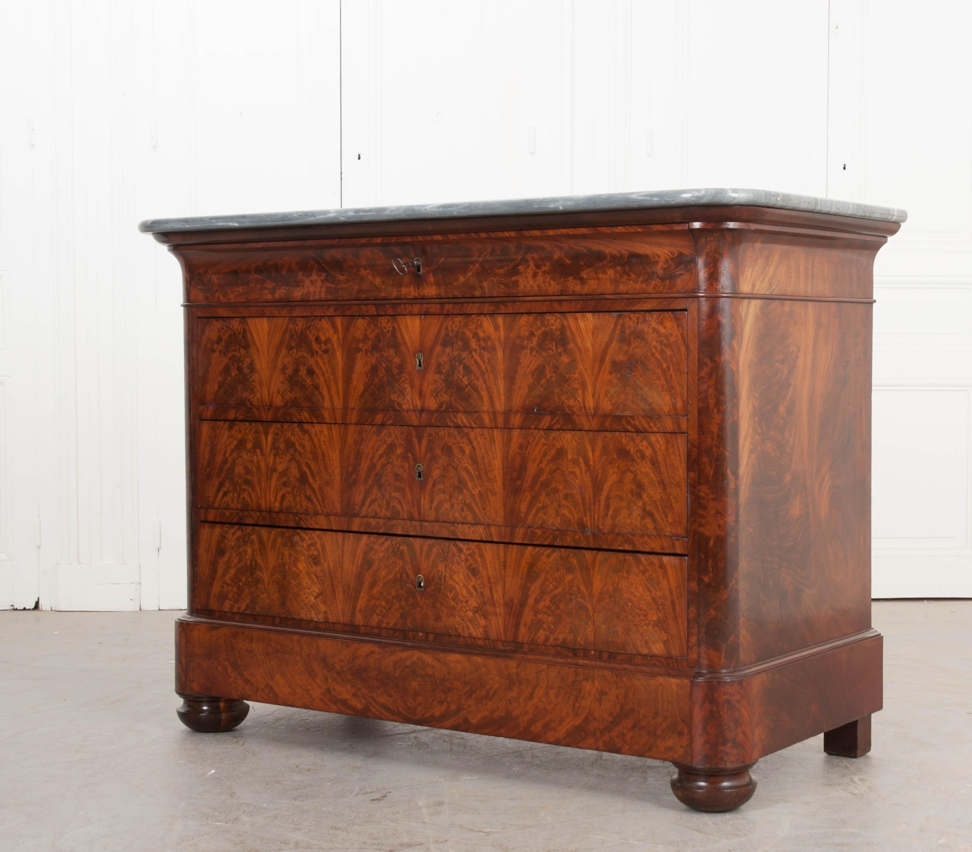This elegant and restrained Louis Philippe flame mahogany four-drawer commode, circa 1830s is from France and has a gorgeous grey marble top and book-matched veneer. The finish is warm and rich with a professional French polish. This elegant piece