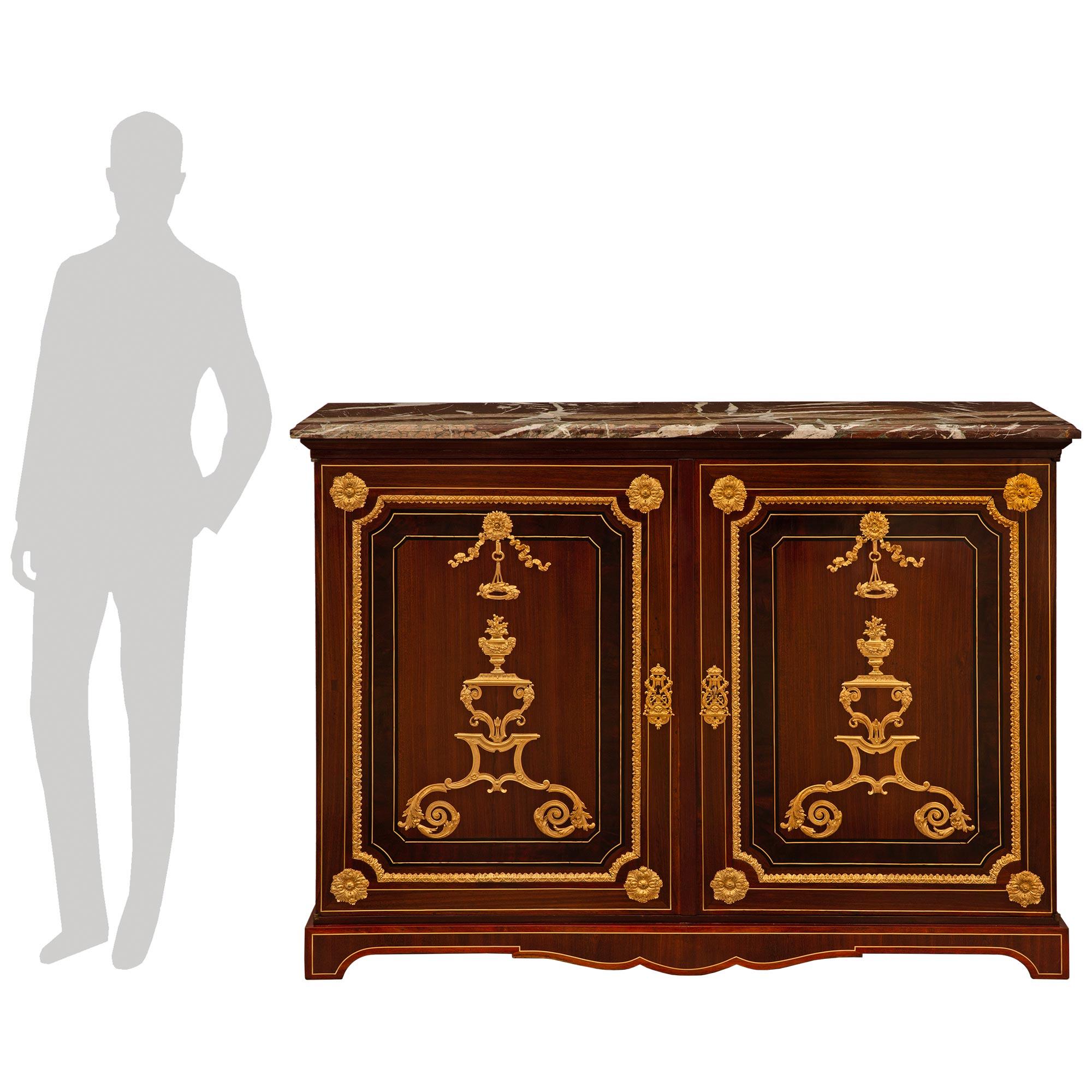 A stunning and very high quality French 19th century Louis XIV st. Mahogany, Kingwood, Palisander, Brass, Ormolu, and Campan Rubané marble cabinet. This exquisite two door two shelf cabinet is raised on a short arbalest shaped base consisting of