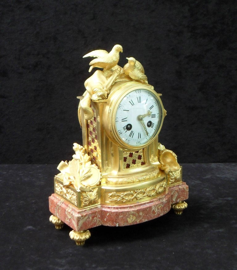 An extremely good quality French Louis XIV style bronze gilt mantel clock with pierced sound frets, musical instruments, soldiers helmet and shield surmounted by two doves on a rouge and white mottled marble plinth base.

The clock has a white