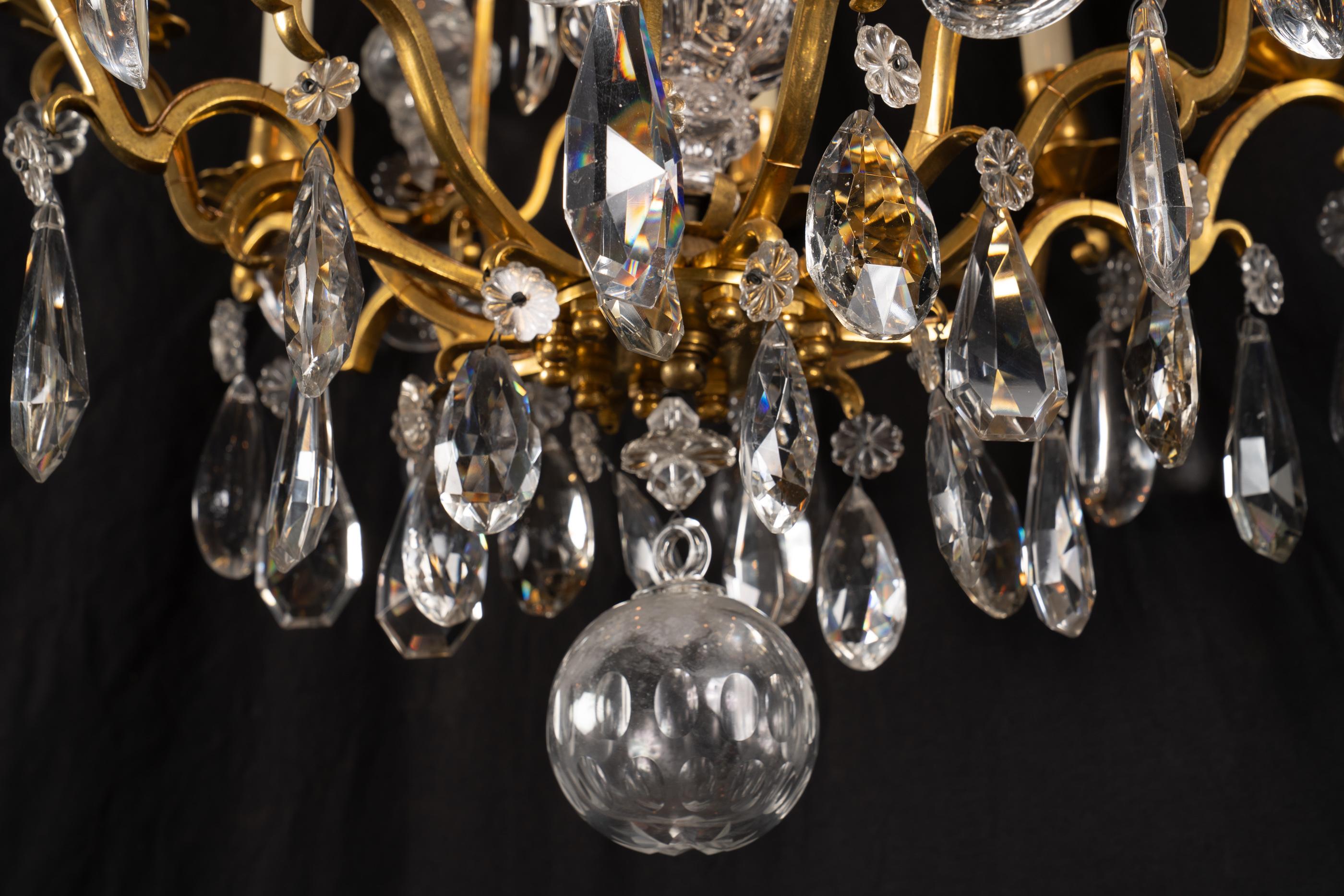 Questo bellissimo lampadario francese del XIX secolo Luigi XV in bronzo e cristallo è ornato da raffinate plaquette di cristallo e nove luci. Il lampadario è caratterizzato da cristalli trasparenti a forma di goccia insieme a cristalli tagliati di