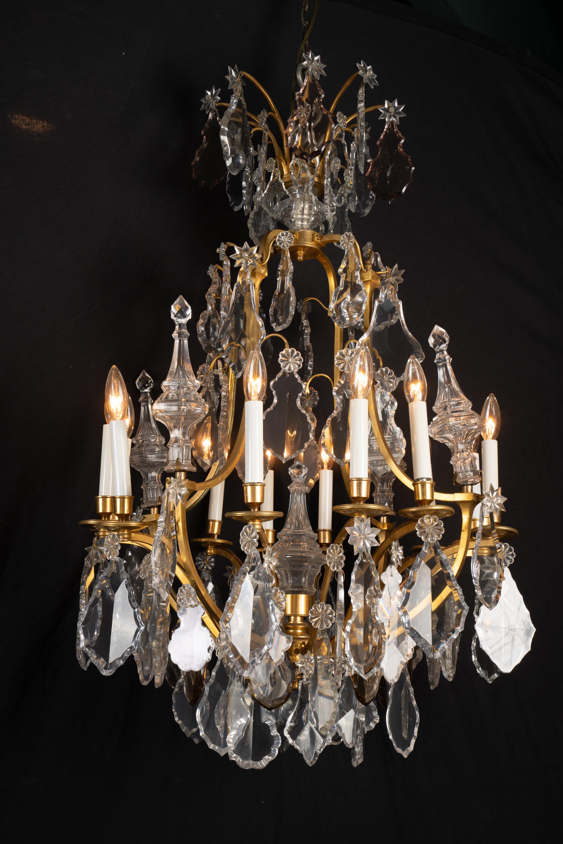 This Louis XV bronze chandelier features bronze candle cups and bobeches along with a plethora of fine crystal. The French antique piece dates back to the 19th century and is draped with clear and rose cut-crystal plaquettes of various shapes