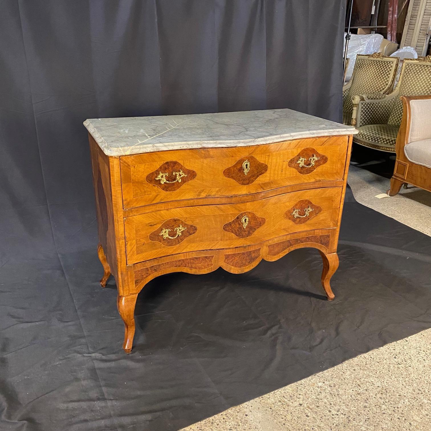 Diese Kommode ist ein elegantes, raffiniertes Beispiel für die Handwerkskunst des 19. Jahrhunderts, inspiriert vom klassischen Stil Louis XV. Die Kommode ist aus wunderschön gemasertem, furniertem Nussbaumholz gefertigt und zeichnet sich durch