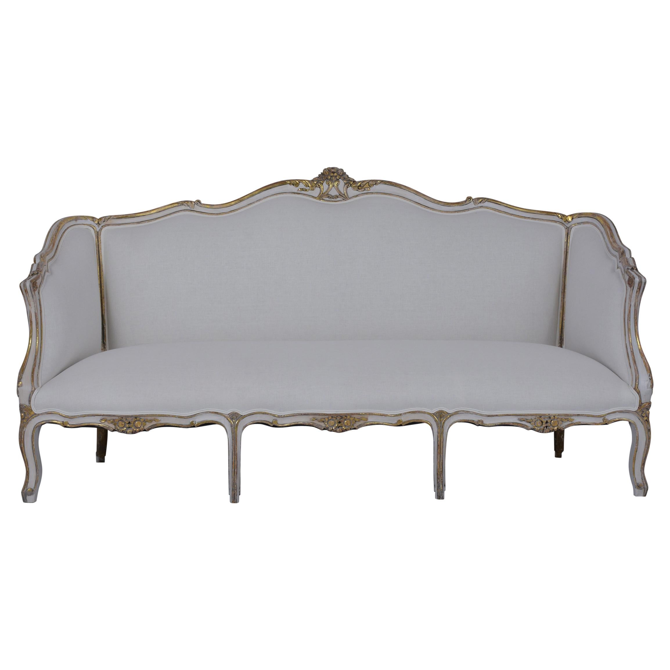 An extraordinary french antique sofa crafted out of walnut wood and has been completely restored. This beautiful sofa features hand-carved details throughout the frame, is finished with a beautiful gilt & painted finish, and has been newly