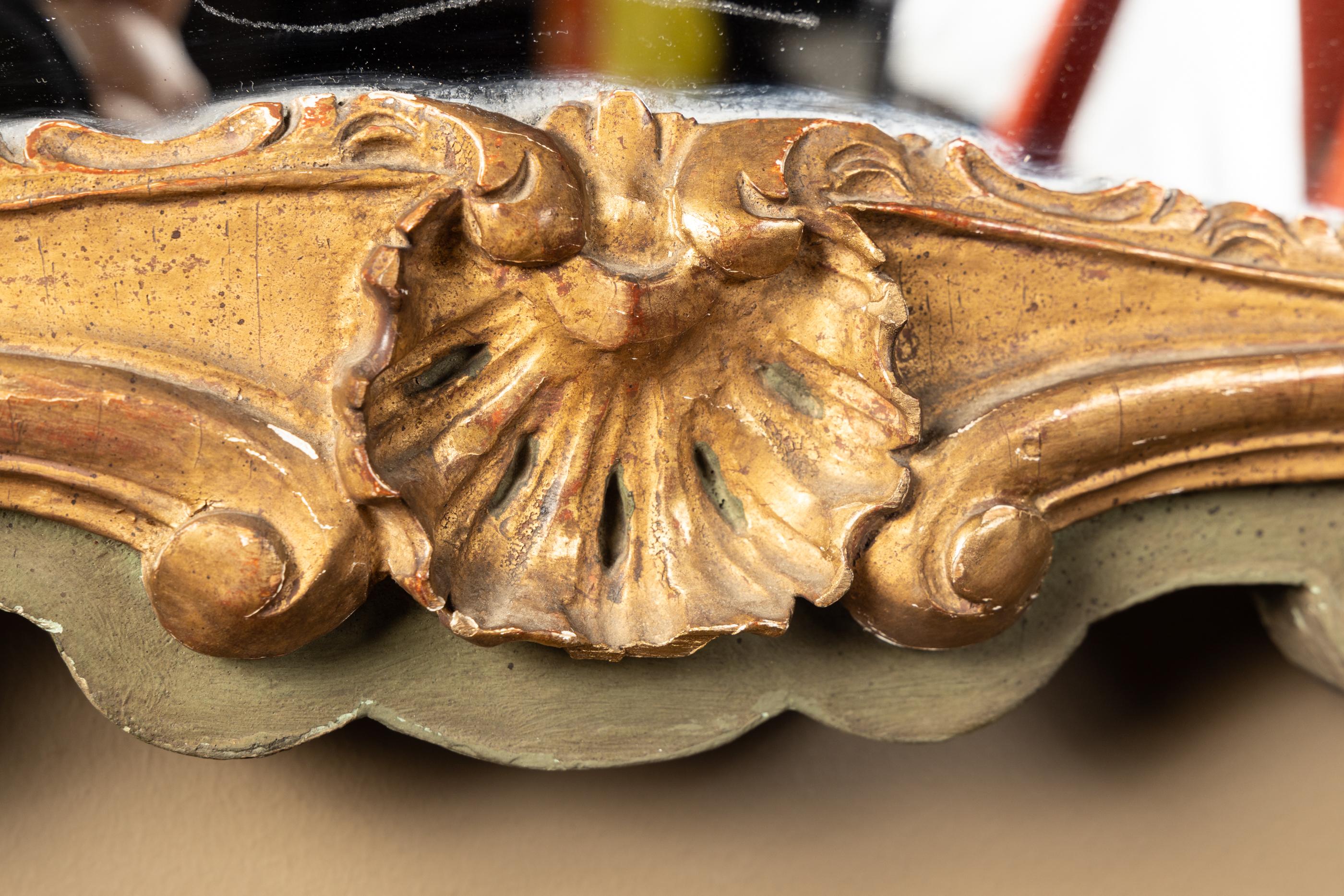 This French Louis XV carved mirror features gold leaf work and dates back to the 19th century. The carved Louis XV details are set on an olive green backdrop. Note the acanthus leaves at top right and left, as well as the garland work which