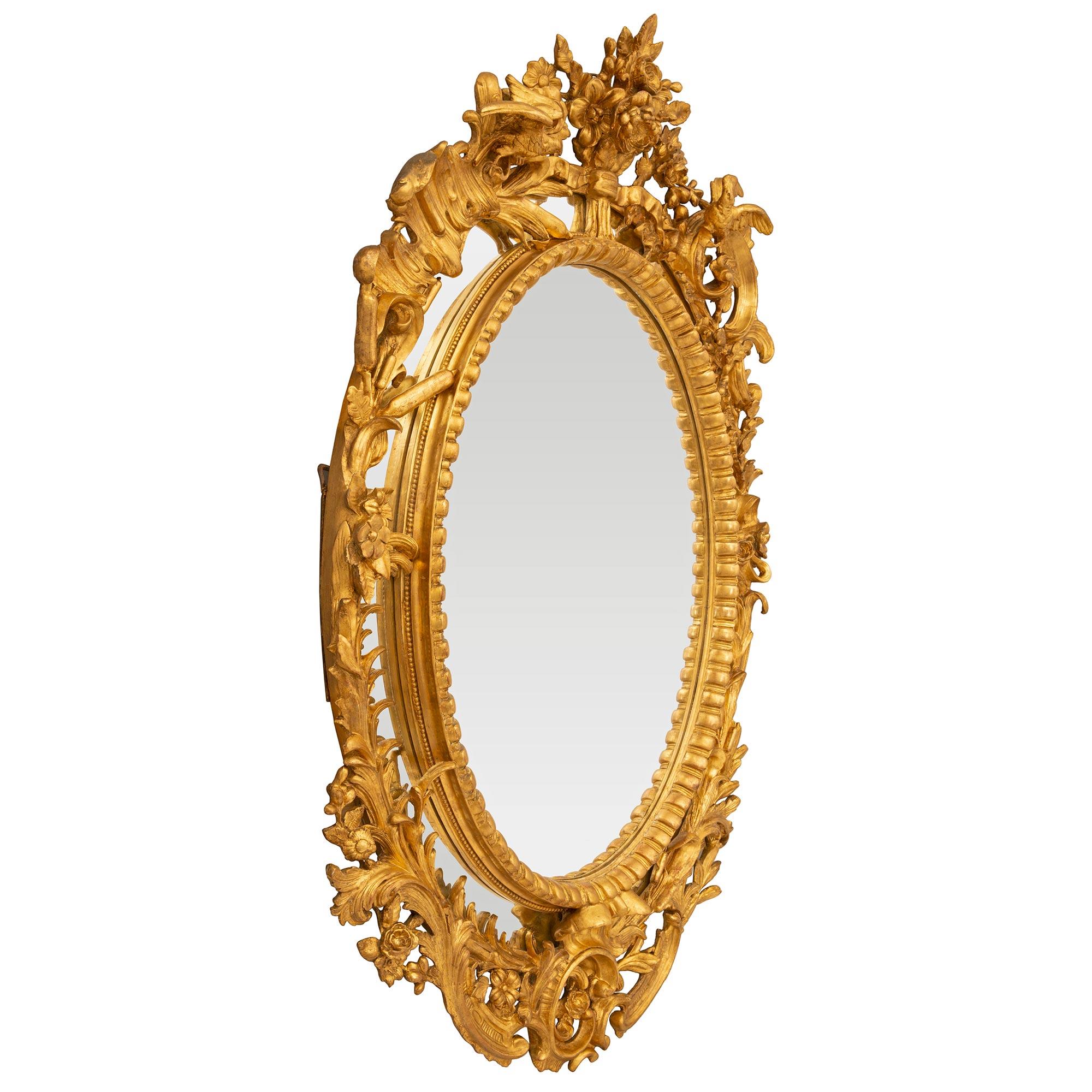 Uno splendido e impressionante specchio francese del XIX secolo in stile Luigi XV con doppia cornice in legno dorato. Lo specchio ovale di grandi dimensioni conserva tutte le lastre di specchio originali, con la lastra di specchio centrale