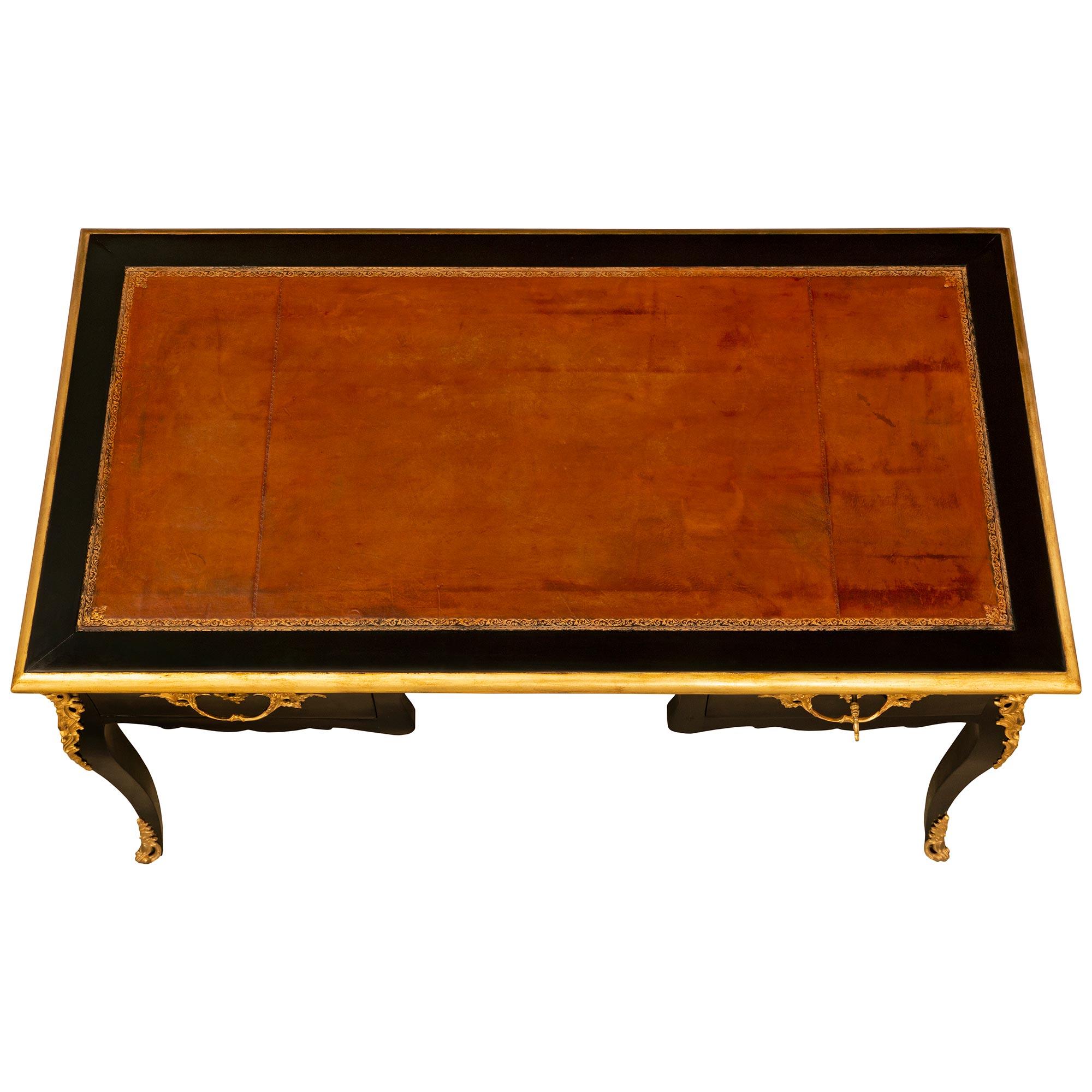 An elegant French 19th century Louis XV st. ebonized Fruitwood and ormolu desk. The Bureau Plat is raised by slender cabriole legs with pierced ormolu sabots decorated with acanthus leaves, a front cartouche and above with pierced ormolu mounts of