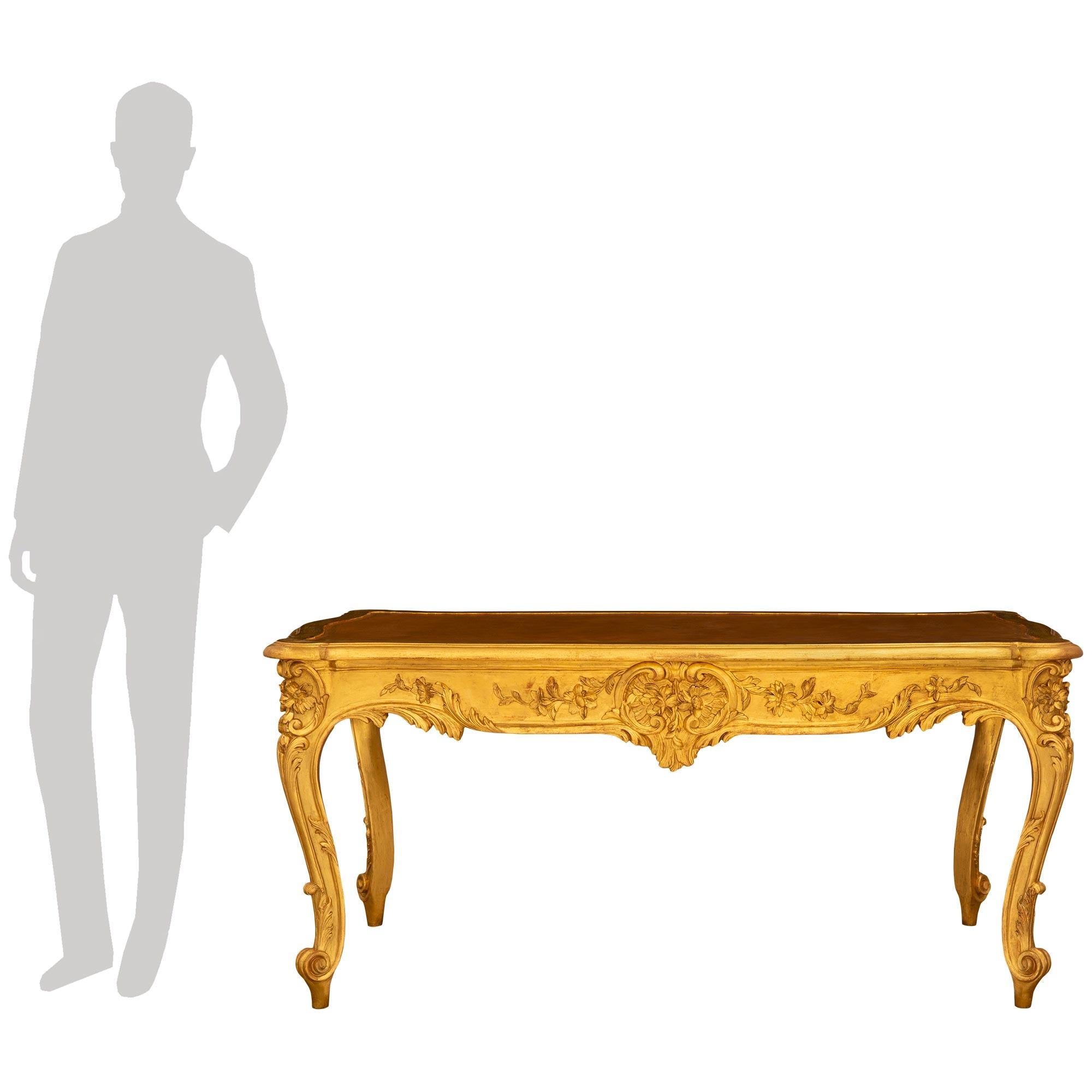 Exceptionnelle et très impressionnante table centrale/de bureau en bois doré et cuir de style Louis XV du 19ème siècle. Cette merveilleuse table rectangulaire repose sur quatre pieds cabriole élancés et richement sculptés, ornés de feuilles