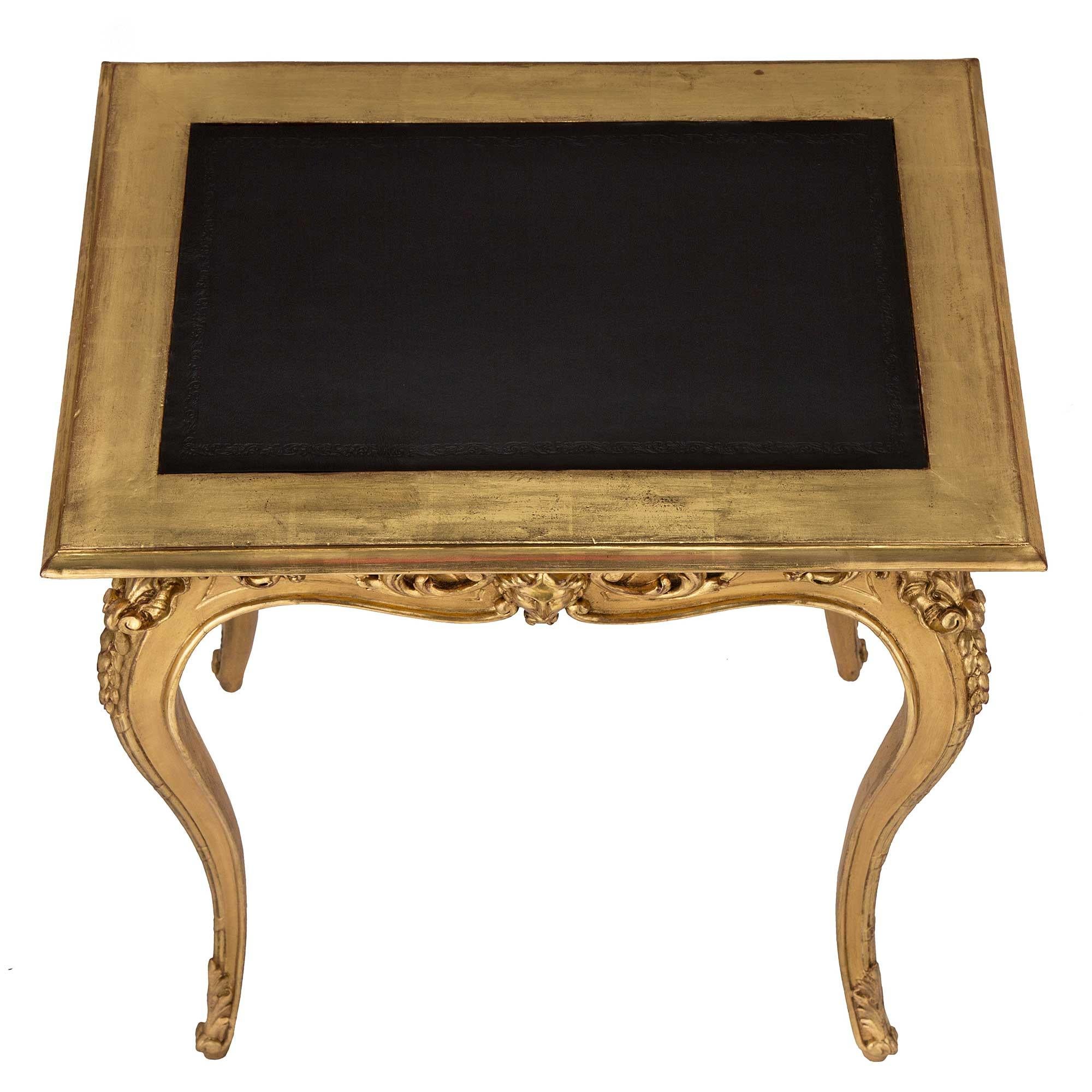 A beautiful and most elegant French 19th century Louis XV st. Giltwood and leather side table. The table is raised by slender cabriole legs with scrolled acanthus leaf feet. The arbalest shaped apron is centered by a richly carved mask of a