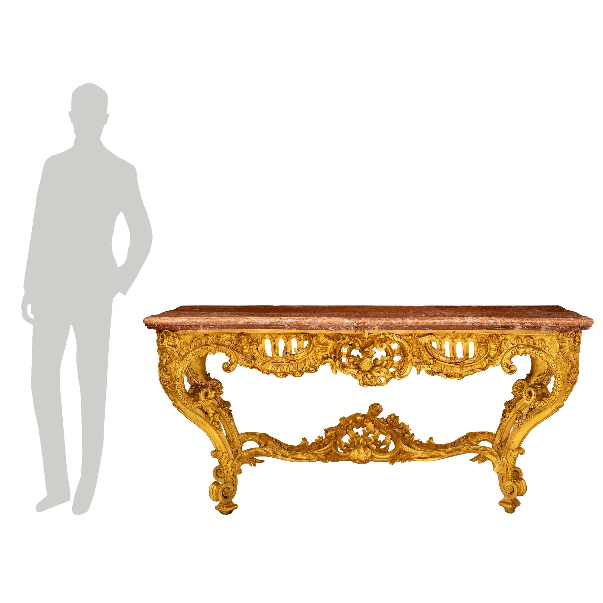 A stunning and most impressive French 19th century Louis XV st. giltwood and Rouge de Languedoc marble console. The freestanding console is raised by beautiful tapered cabriole legs with fine square feet and striking scrolled richly carved acanthus