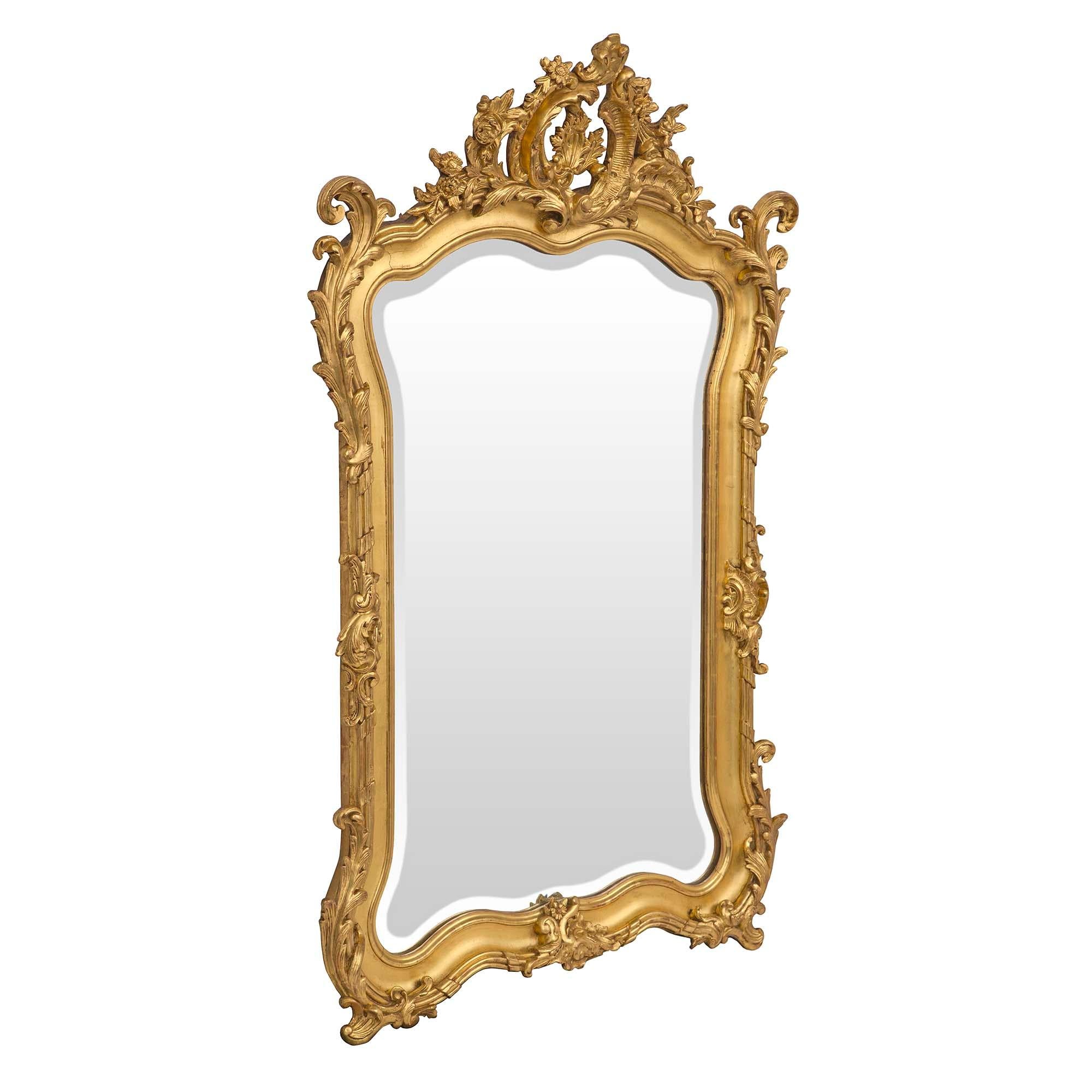 An exceptional French 19th century Louis XV st. giltwood mirror. The original beveled mirror plate is framed within an elegant curved border with two scrolled foliate bottom feet centering a finely carved reserve. Running along the side throughout