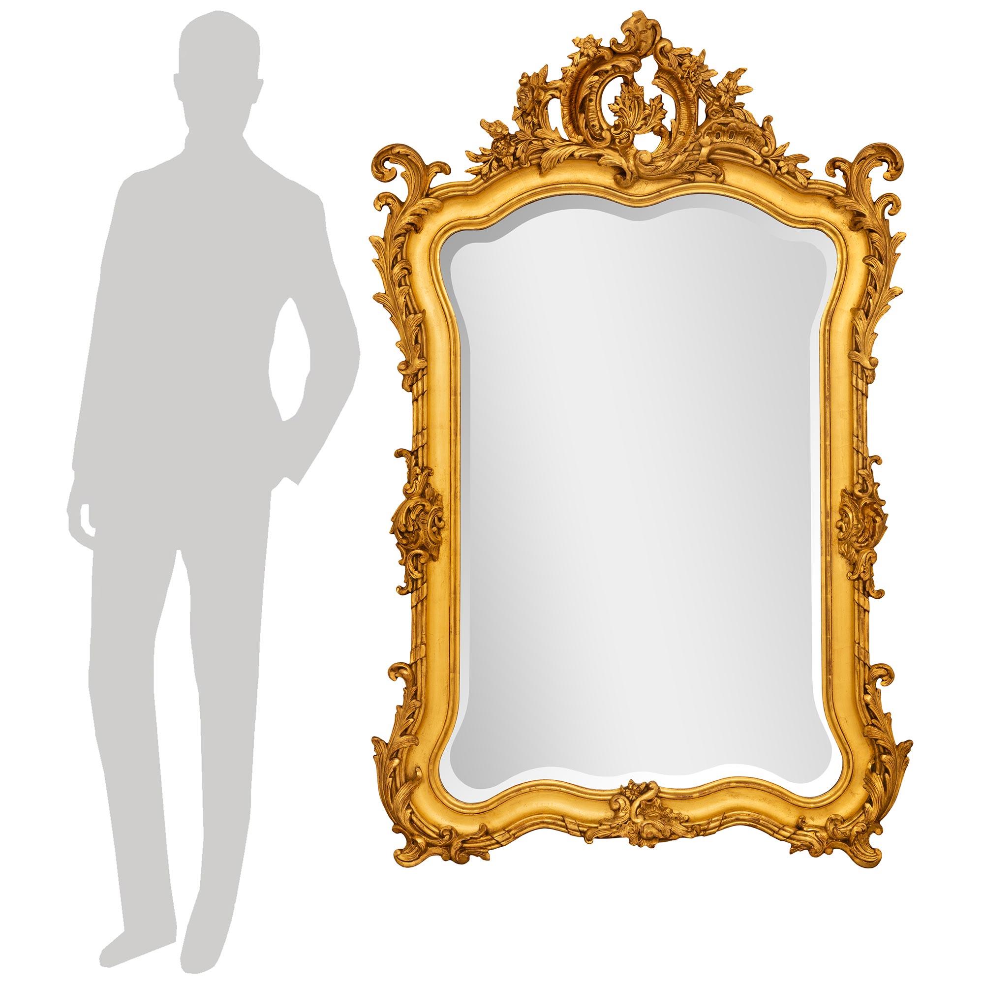 Un eccezionale specchio in legno dorato francese del XIX secolo Luigi XV di alta qualità. L'originale lastra a specchio smussata è incorniciata da un elegante bordo curvo con due piedi inferiori a volute foliate che centrano una riserva finemente