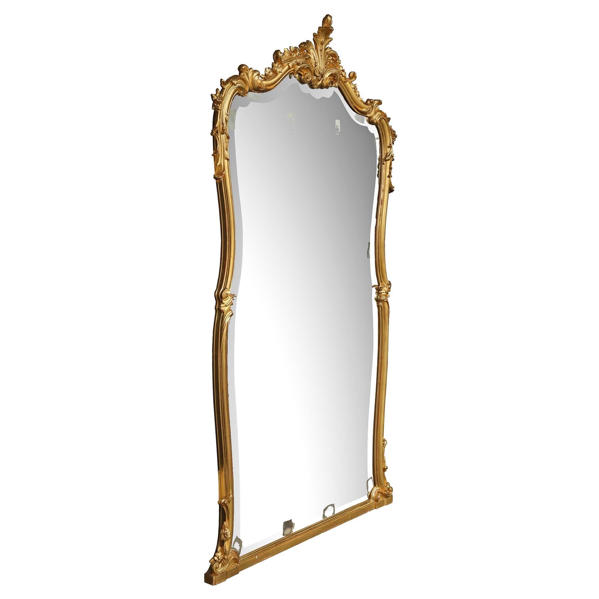 An elegant French 19th century Louis XV st. giltwood mirror. The original beveled mirror plate is framed within an extremely decorative scrolled moulded giltwood border. At the border are floral carvings and a straight bottom support. The rich top