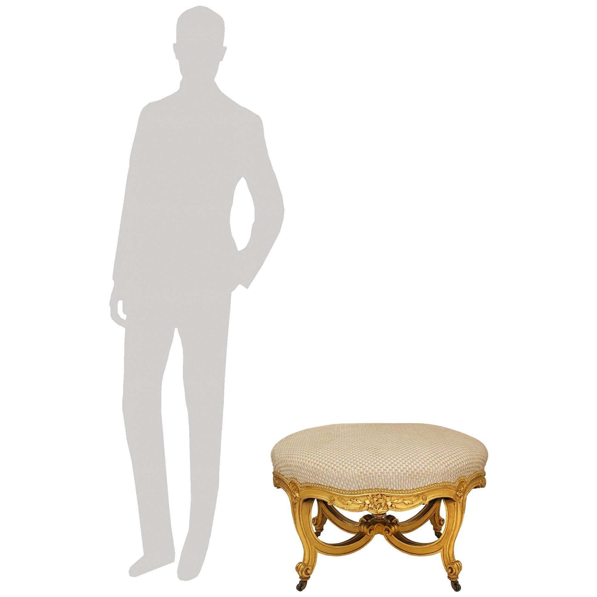 Elegante taburete de madera dorada estilo Luis XV francés del siglo XIX, de gran calidad. Este encantador taburete circular se eleva sobre cuatro patas con volutas y cuentas, apoyadas en las ruedas originales de latón. Cada una de las patas,