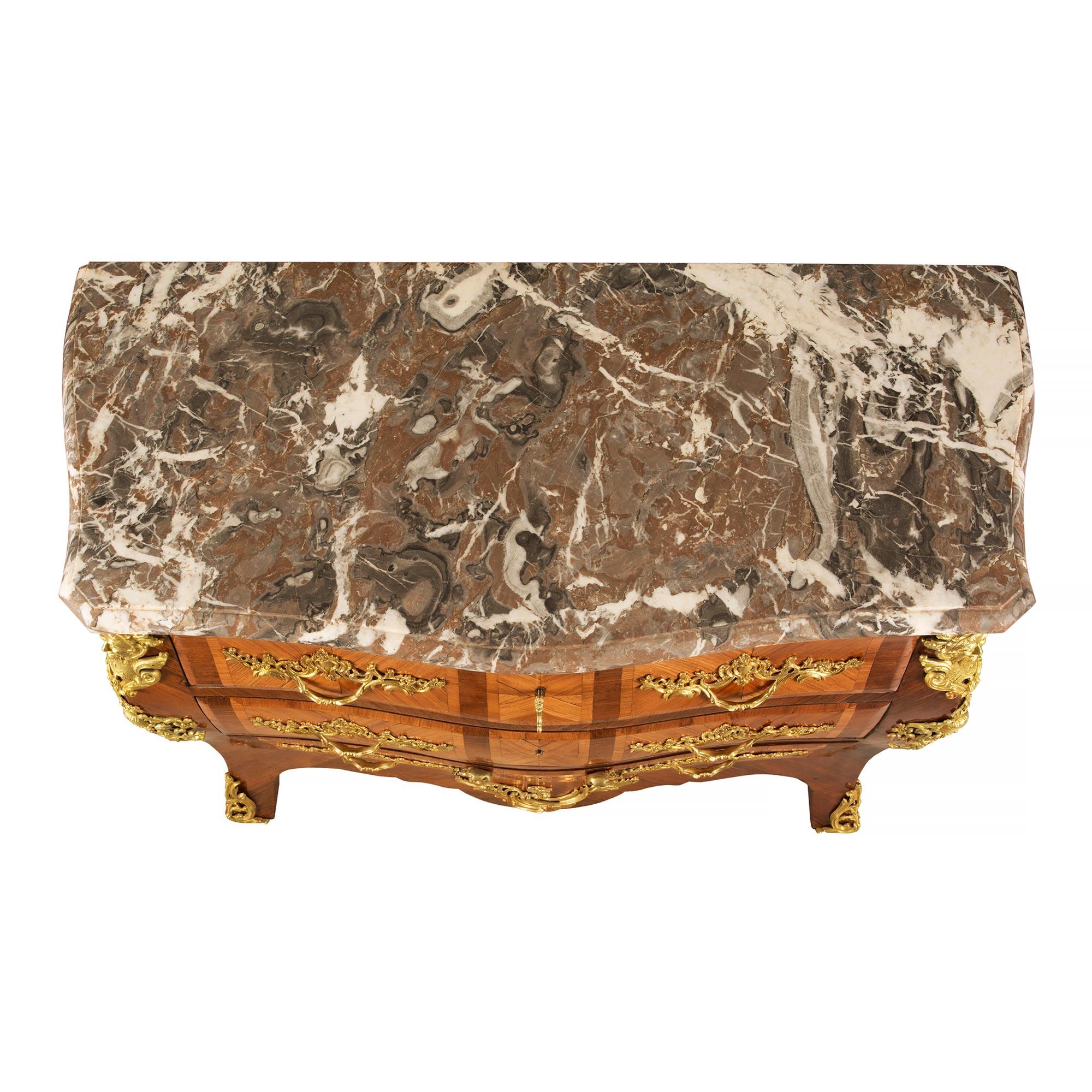 A stunning French 19th century Louis XV st. three drawer kingwood, tulipwood and ormolu commode. The bombe shaped commode is raised on short cabriole legs decorated by ormolu masculine masks above scrolled mounts. The scrolled shaped frieze is