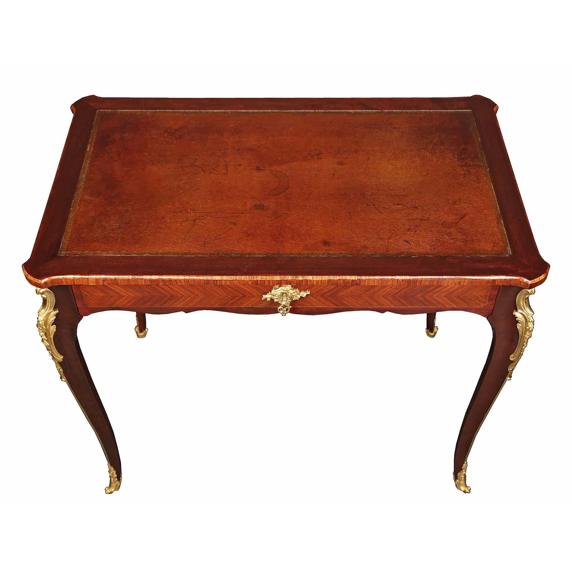 An elegant French 19th century Louis XV st. mahogany one drawer desk. The desk is raised by four slender, elegant cabriole legs with highly chased ormolu foliate mounts at the top, chutes, and wrap-around sabots. The single wide drawer with inlaid
