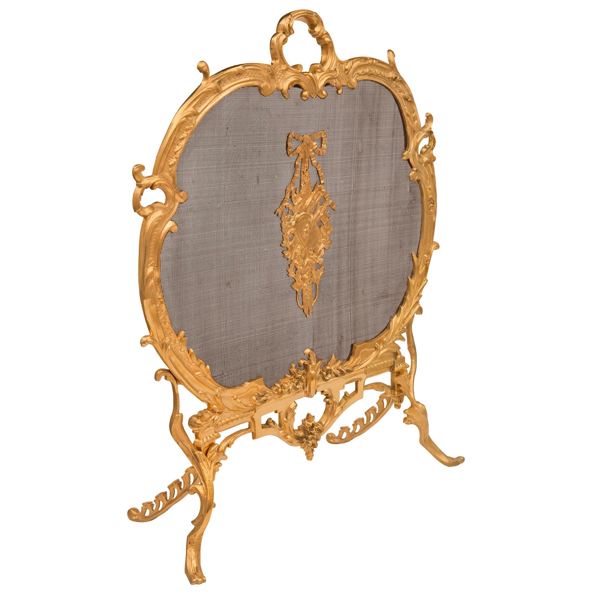 A striking French 19th century Louis XV st. ormolu and mesh fire screen. The fire screen is raised by beautiful scrolled foliate legs in the shape of acanthus leaves seemingly growing upwards centering a beautiful floral reserve with charming richly