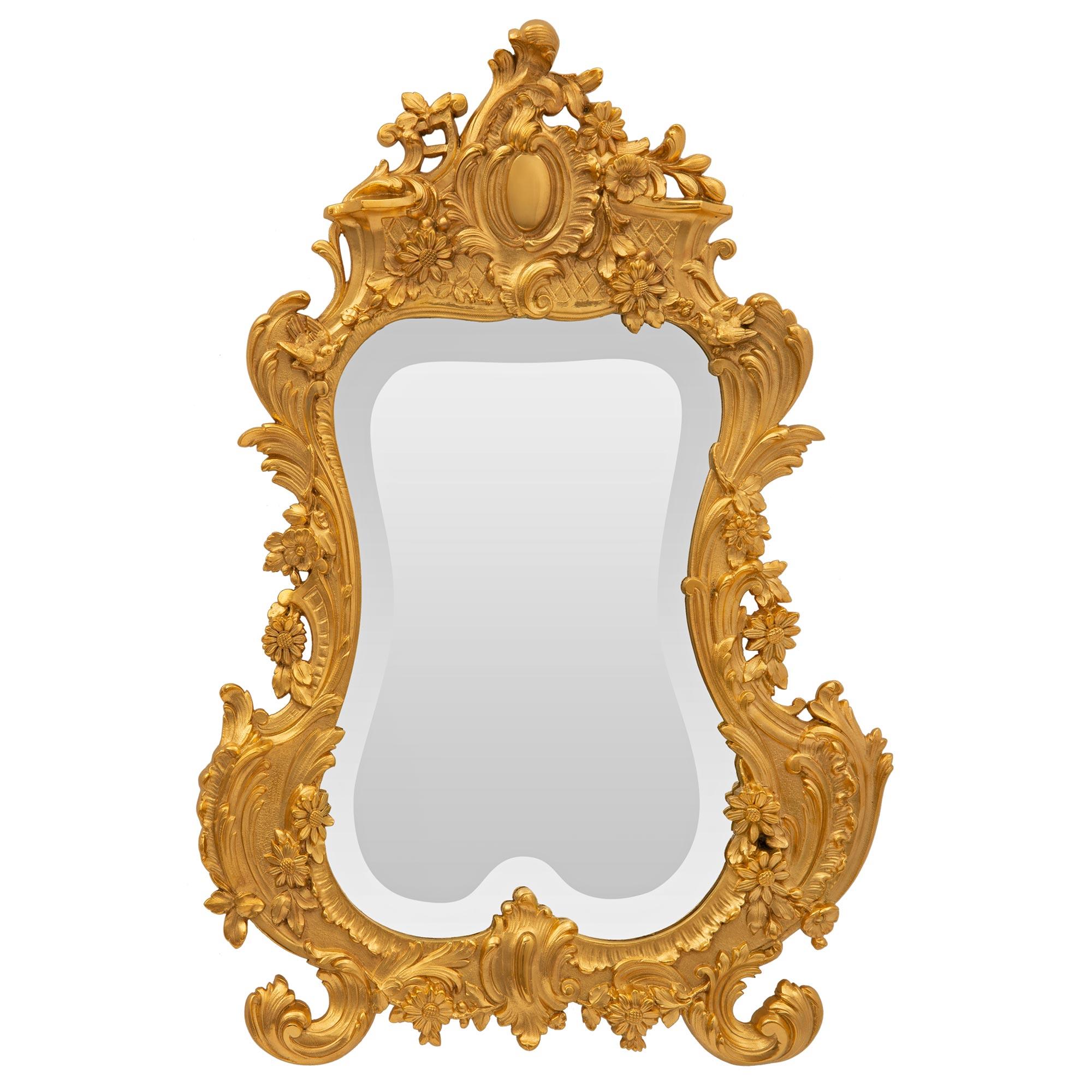 A charming and high quality French 19th century Louis XV st. ormolu vanity mirror. The small scale wall mounted mirror retains its original beautiful beveled mirror plate set within the striking ormolu frame. The frame displays a most decorative