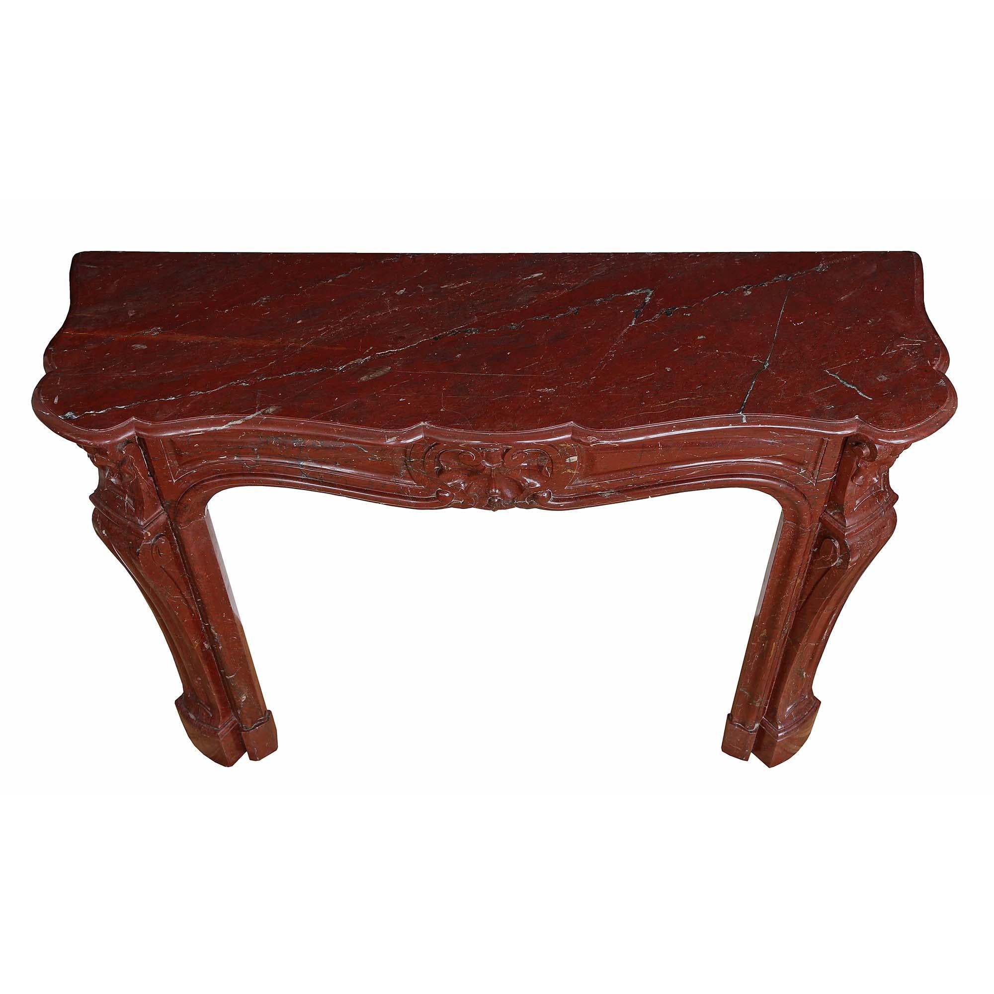 Un delizioso caminetto francese del XIX secolo in stile Luigi XV st. Rouge Griotte. Gli stipiti a voluta sorreggono un fregio a raggiera con una riserva centrale di conchiglie Rocaille estremamente ben intagliata all'interno di un disegno di bordo