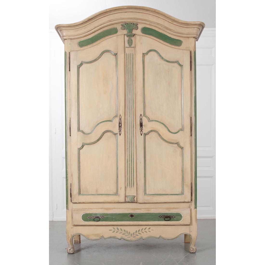 This is an outstanding, painted French Provincial armoire with Chapeau de Gendarme cornice. Soft creamy-beige body color with green highlighting the details and adding character to this piece. There are two doors with shapely carved panels creating