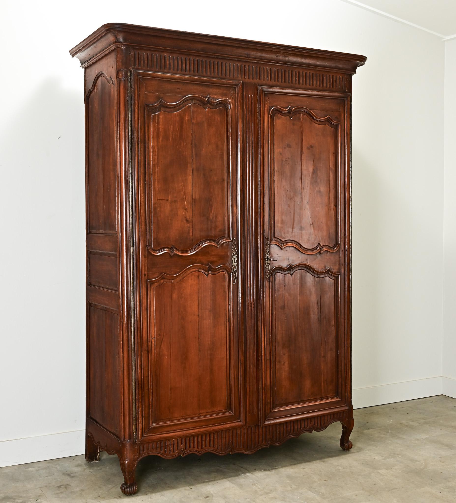 Grande armoire de style Louis XV en noyer massif sculpté. Vous trouverez des sculptures géométriques sous la corniche et sur le tablier festonné. L'impressionnante paire de portes d'armoire sculptées et lambrissées est suspendue à des charnières en