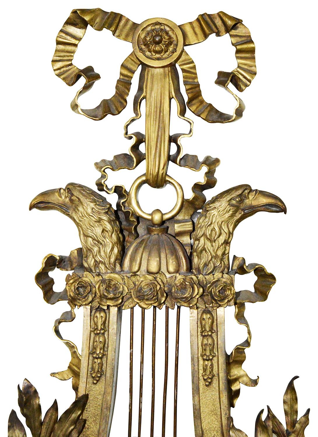 A wonderful, classical Empire influenced 19th century gilded ormolu Cartel wall clock, having ribbon and scrolling foliate decoration. The white enamel clock face set in a Lyre with a pair of stylised Eagles heads. The clock strike on the hour and