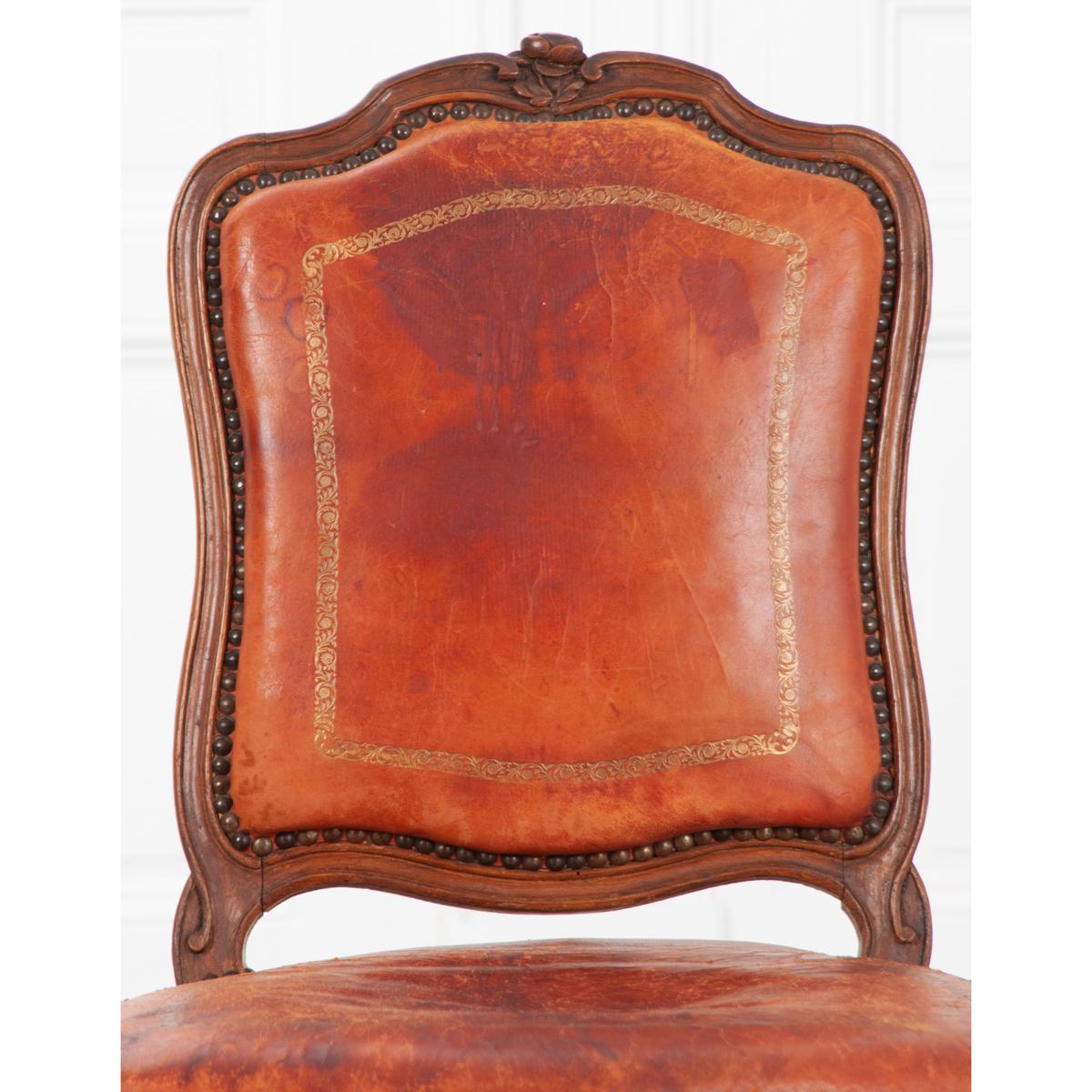 A stunning Louis XV style chair, upholstered in a heavily-worn antique leather. The shapely chair has a walnut frame that has patinated over time, acquiring an amazing antique finish. It has a rose carved into the frame at the top of the backrest
