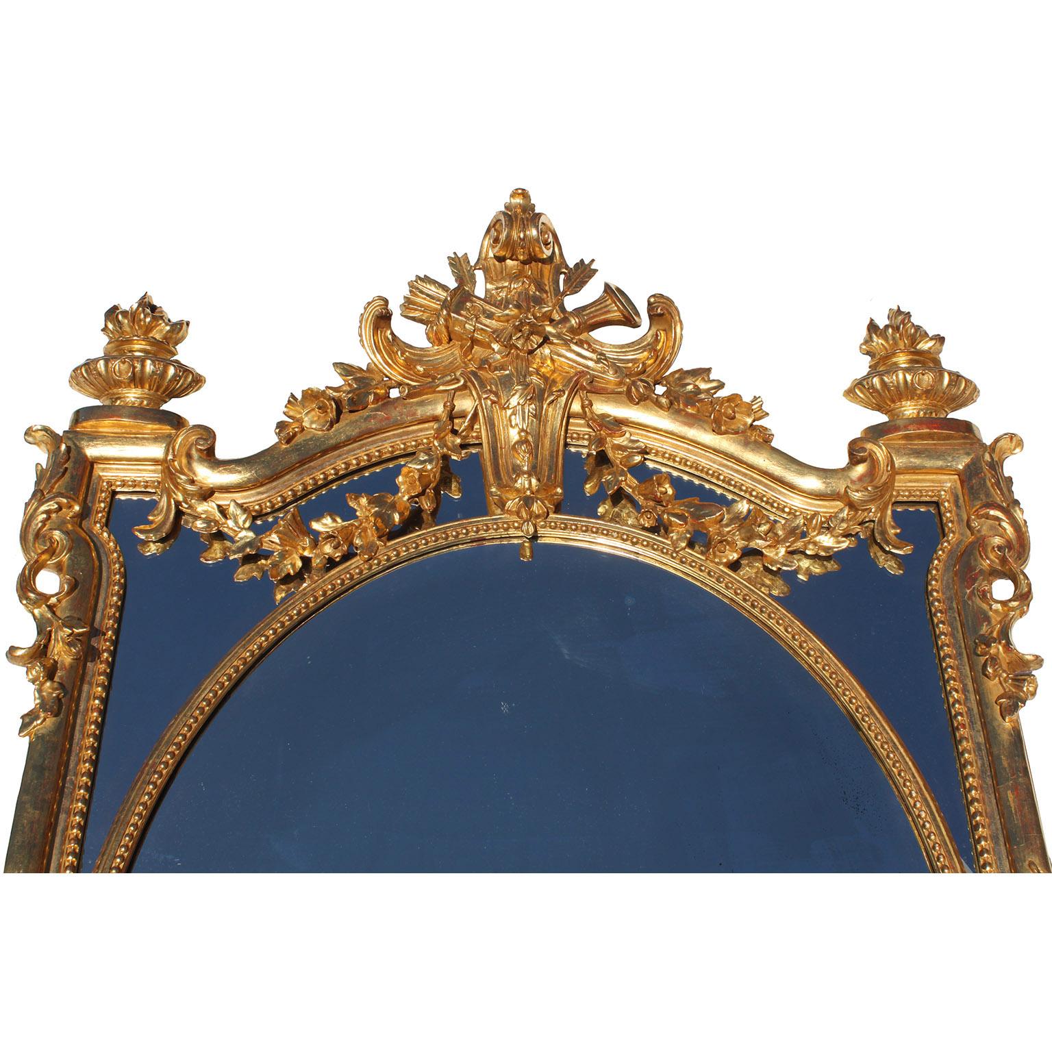 A Very Fine French 19th Century Louis XV Style Gilt-Wood and Gilt-Gesso Carved Ornamental Mantel Mirror. The center oval mirror plate with mirrored corner panels, crowned with an allegorical scrolled carving of an arrow quiver, a flute, arrows,