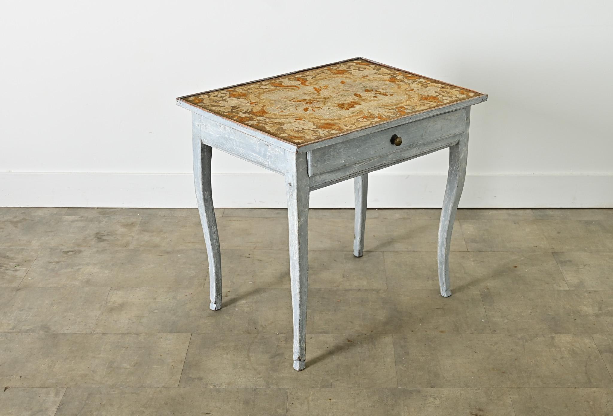 This captivating French 19th century Louis XV-style tea table or side table features a surface covered with an exquisite needlepoint tapestry in shades of ochre and gold on a background of French gray. 
The frame and cabriole legs are washed in a