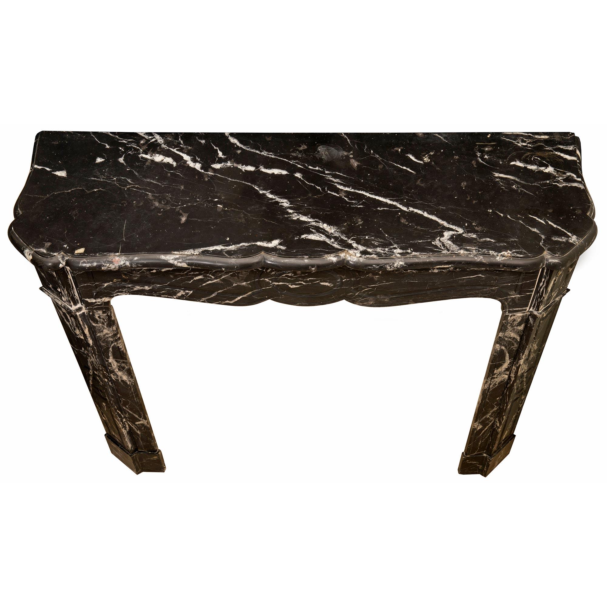 An elegant French 19th century Louis XV st. Noir Antique marble fireplace mantel. The mantel is raised by elegant straight jambs with a mottled base, cut corners and fine circular ormolu air vents. The striking arbalest shaped frieze is centered by