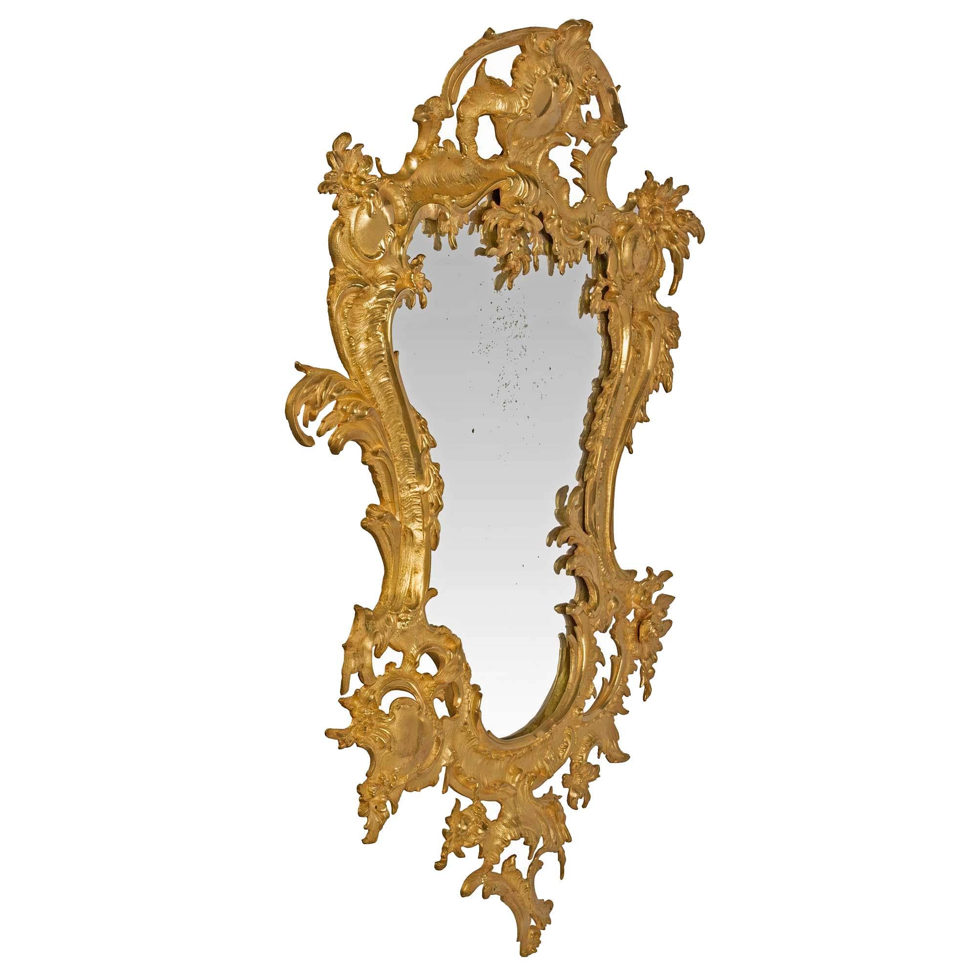 A fanciful small-scale French 19th century Louis XV style ormolu mirror with its original mirror plate. The ormolu frame has a pierced design, with various scrolls amidst foliate and cabochons on both sides, as well as the top central reserve. The