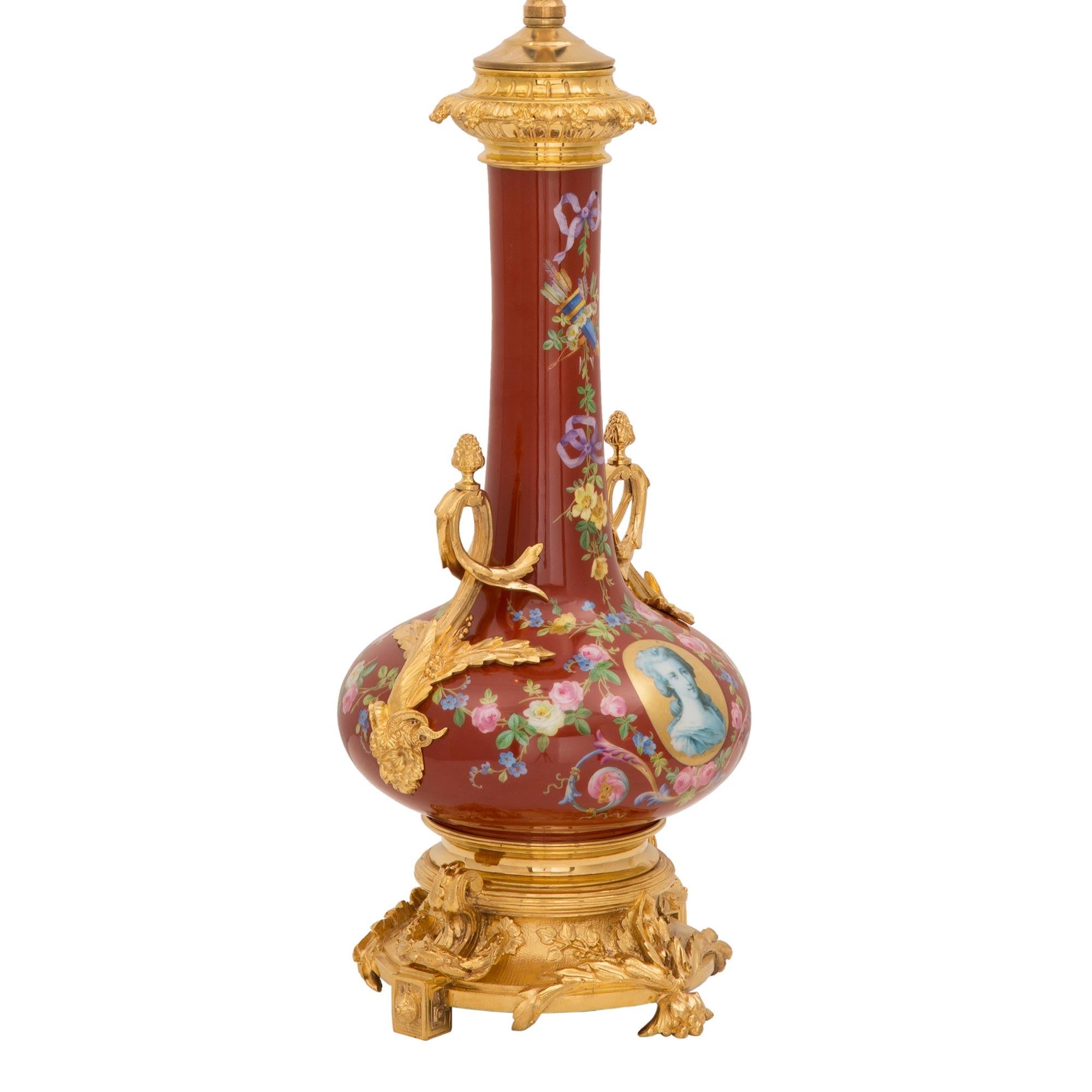 Preciosa lámpara francesa del siglo XIX de porcelana y ormolina de estilo Luis XV. La lámpara se alza sobre una llamativa base de ormolina ricamente cincelada con finos diseños foliados y llaves griegas en acabado satinado y bruñido. El cuerpo de