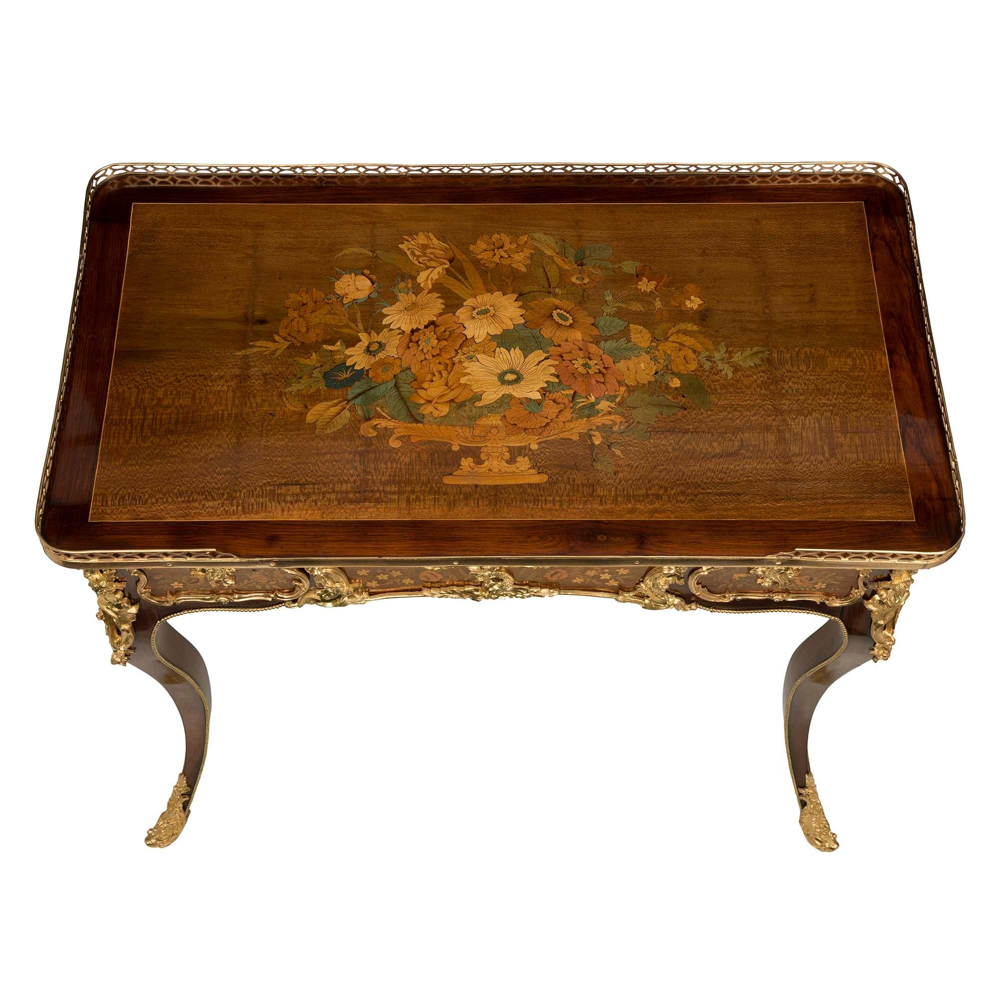 An elegant French 19th century Louis XV St. Charnwood, tulipwood, and ormolu side table or writing desk. The table is raised by beautiful cabriole legs with fine wrap-around pierced ormolu sabots with a foliate design. A beaded ormolu chute extends