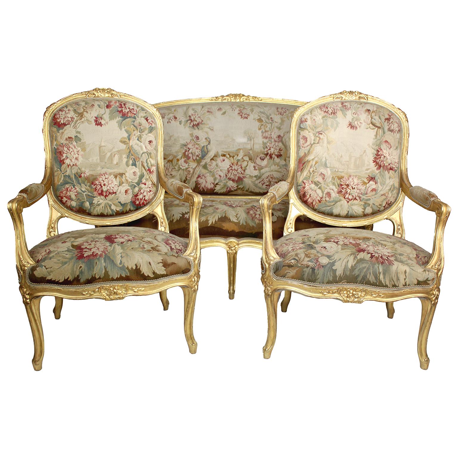 A very fine French 19th century Louis XV style three-piece giltwood carved and silk Aubusson tapestry three-piece salon suite, comprising of a settee and two fauteuils (armchairs), the Aubusson silk tapestry with a design of flowers, trees, parrots
